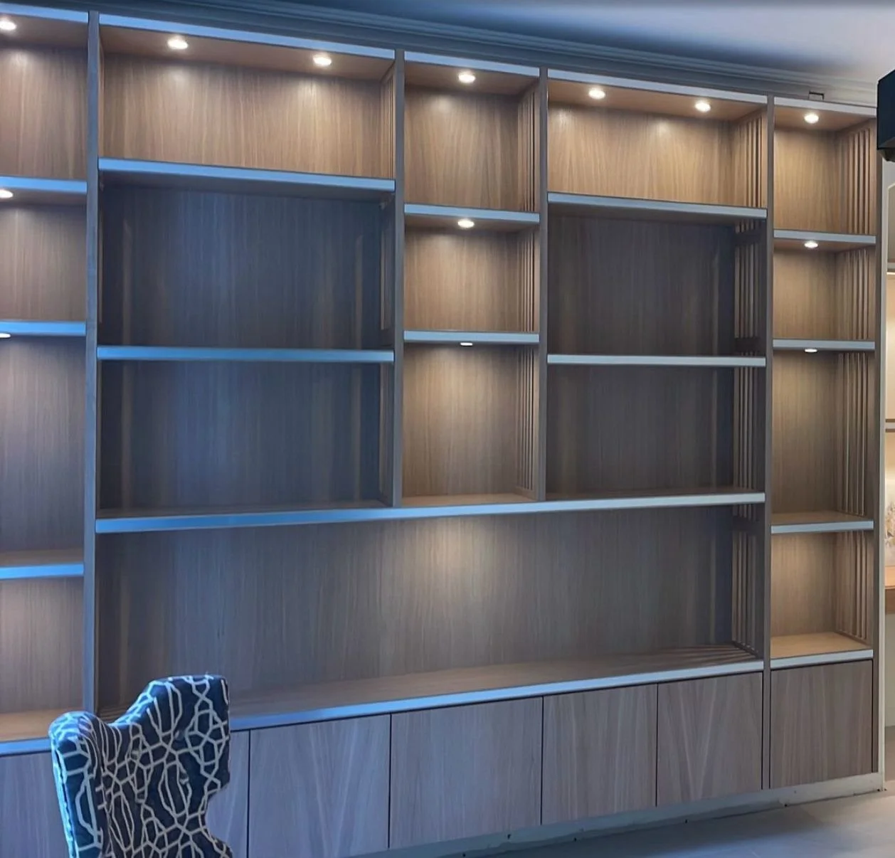 Empty modern wooden bookshelf with built-in lighting, and a patterned chair in the corner.