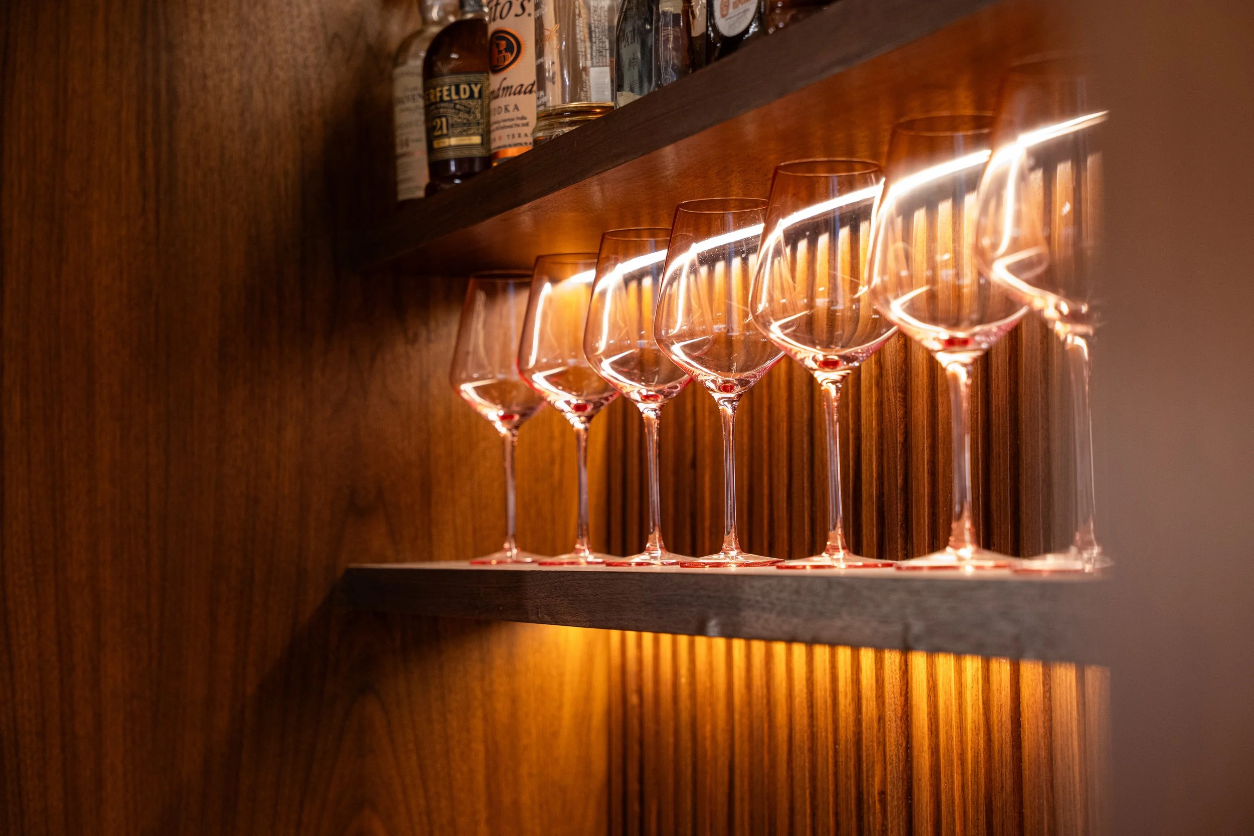 Six empty pink champagne glasses on a wooden shelf under warm lighting.