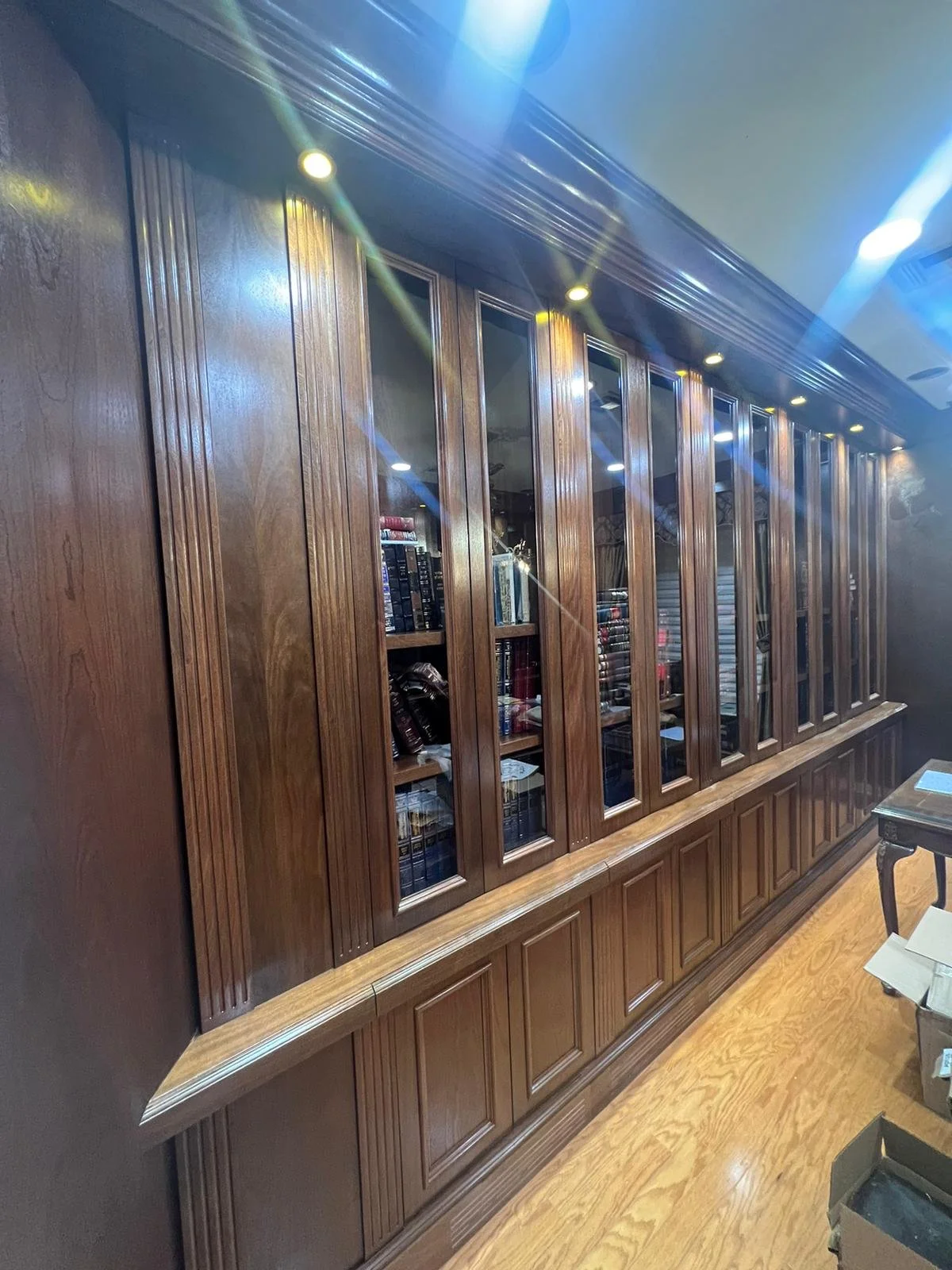 Wooden bookshelf with glass doors and books inside, mounted on a wall with built-in lighting.