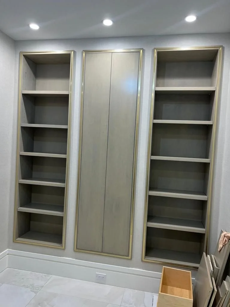 Empty built-in bookshelves and a closed cabinet wall in a room with recessed ceiling lights and light-colored floor tiles.