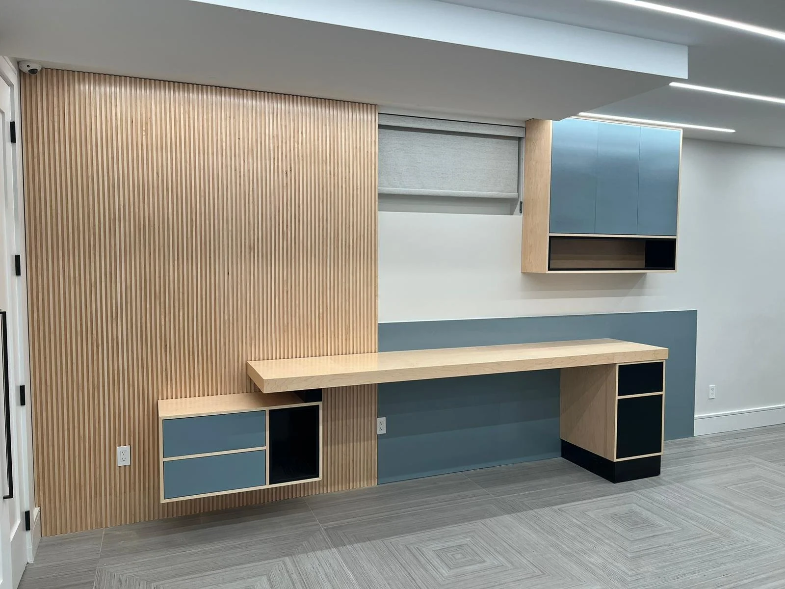 Modern room with a wooden slat wall, floating desk, and built-in cabinets with blue, black, and light wood finishes.