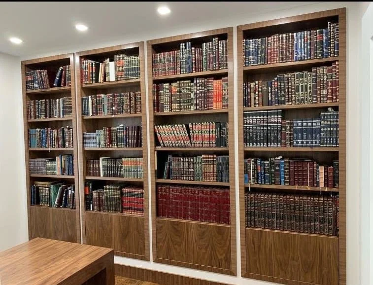 Four wooden bookshelves filled with legal books and texts in a well-lit room, with a wooden table visible in the foreground.