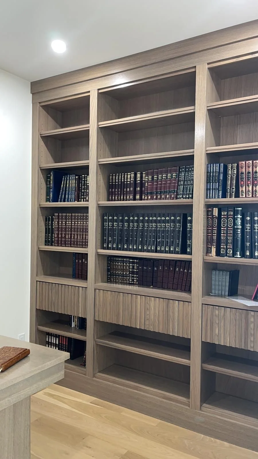 Empty wooden bookshelf with several shelves and some books on the bottom shelves in a room with light-colored flooring and white walls.