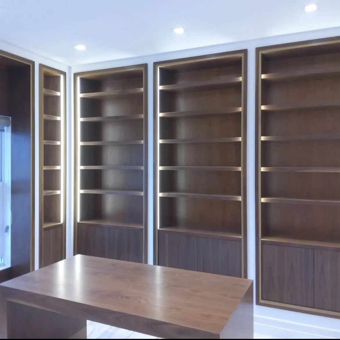 Empty wooden bookshelves in a modern room with a wooden table in the foreground.