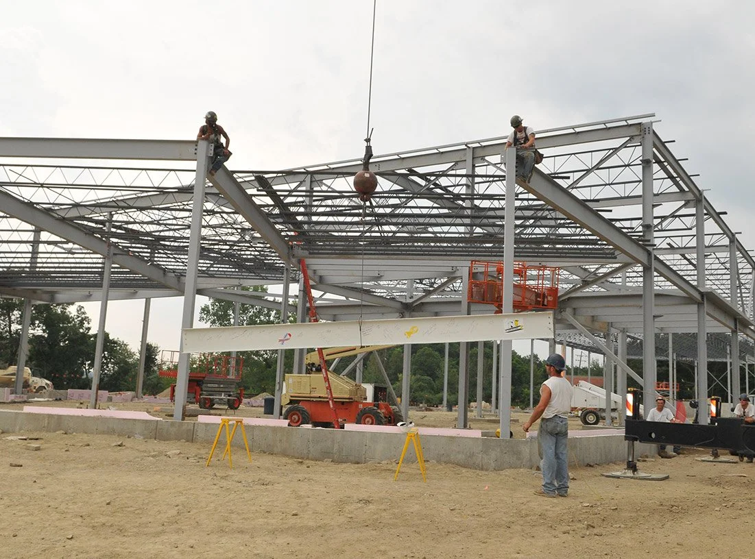 Construction workers on a steel building frame with an overhead crane at a construction site.