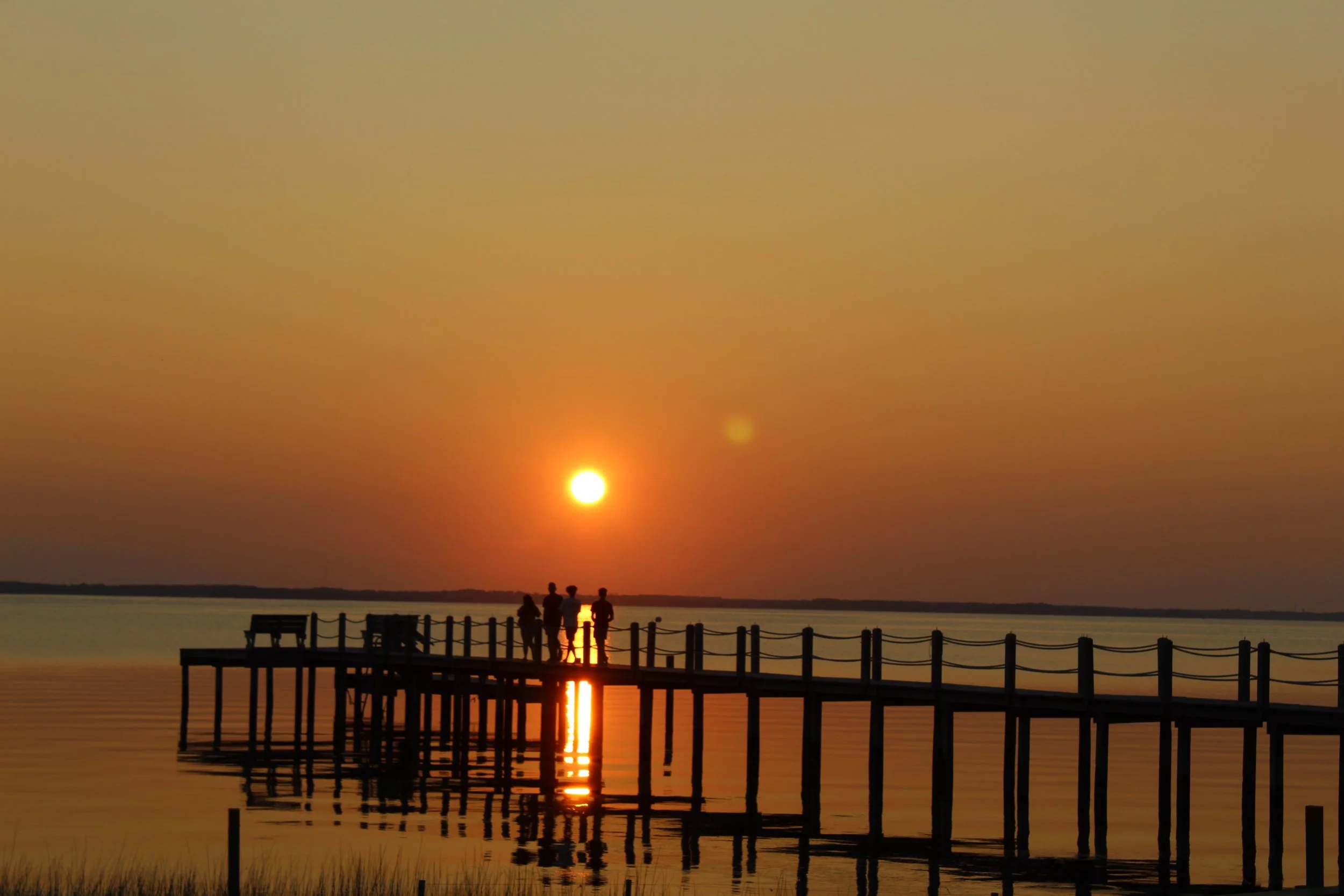 People standing on a wooden pier during sunset over calm water