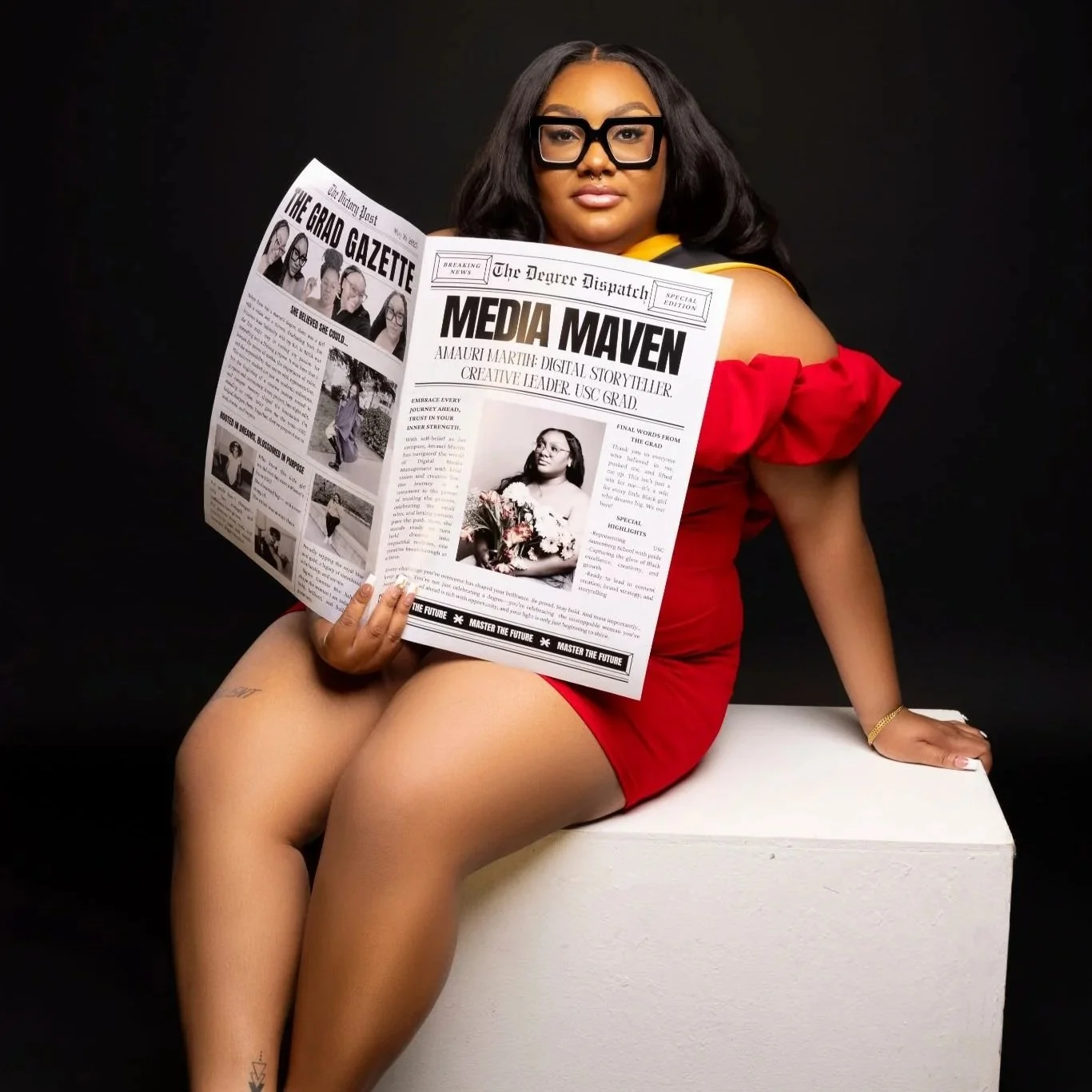 A woman with long dark hair, glasses, and gold jewelry sits on a white block against a black background, holding a newspaper titled 'Media Maven'.