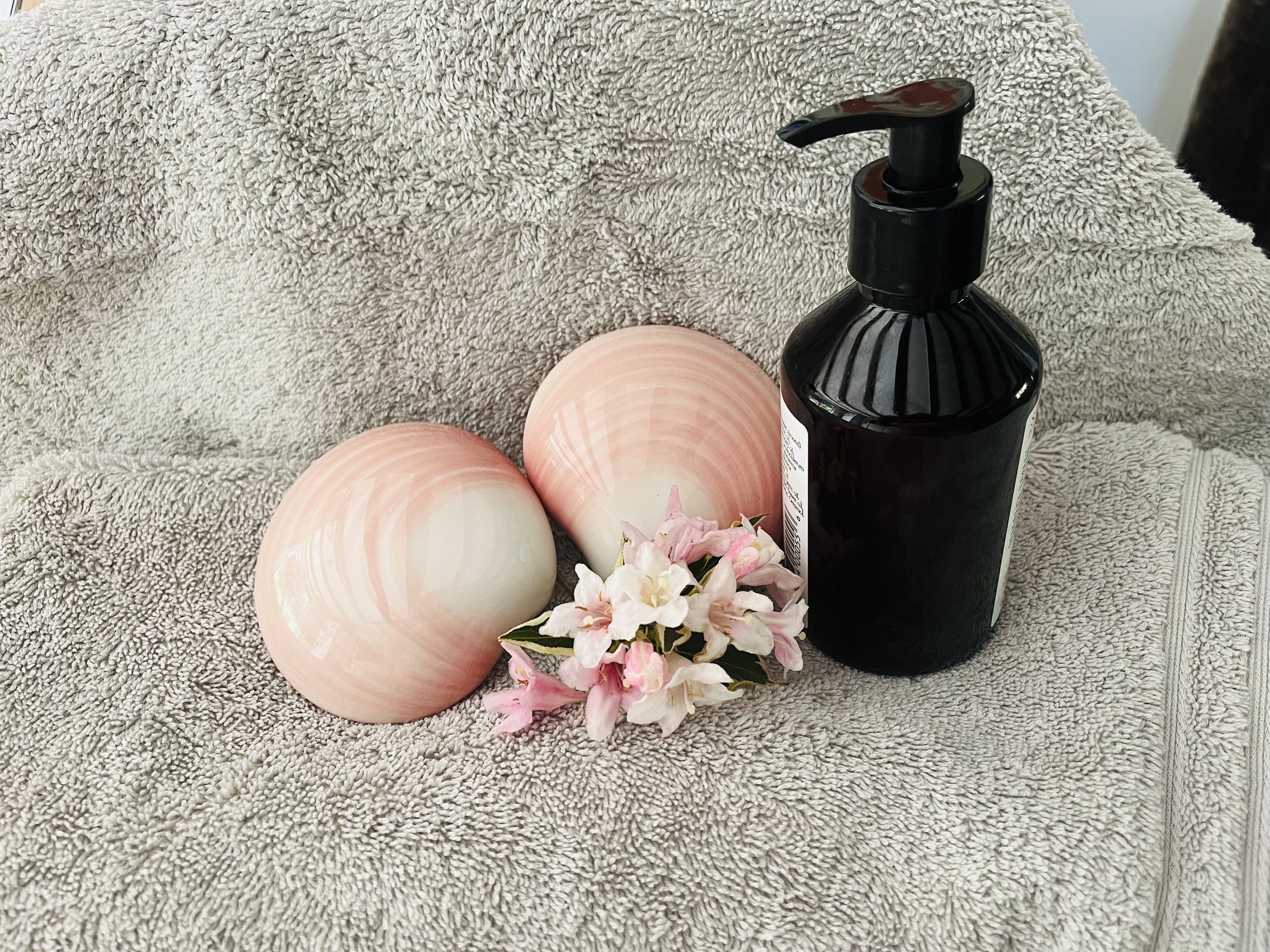 Decorative black soap dispenser, pink and white candles, pink flowers, and a beige textured towel or blanket in the background.