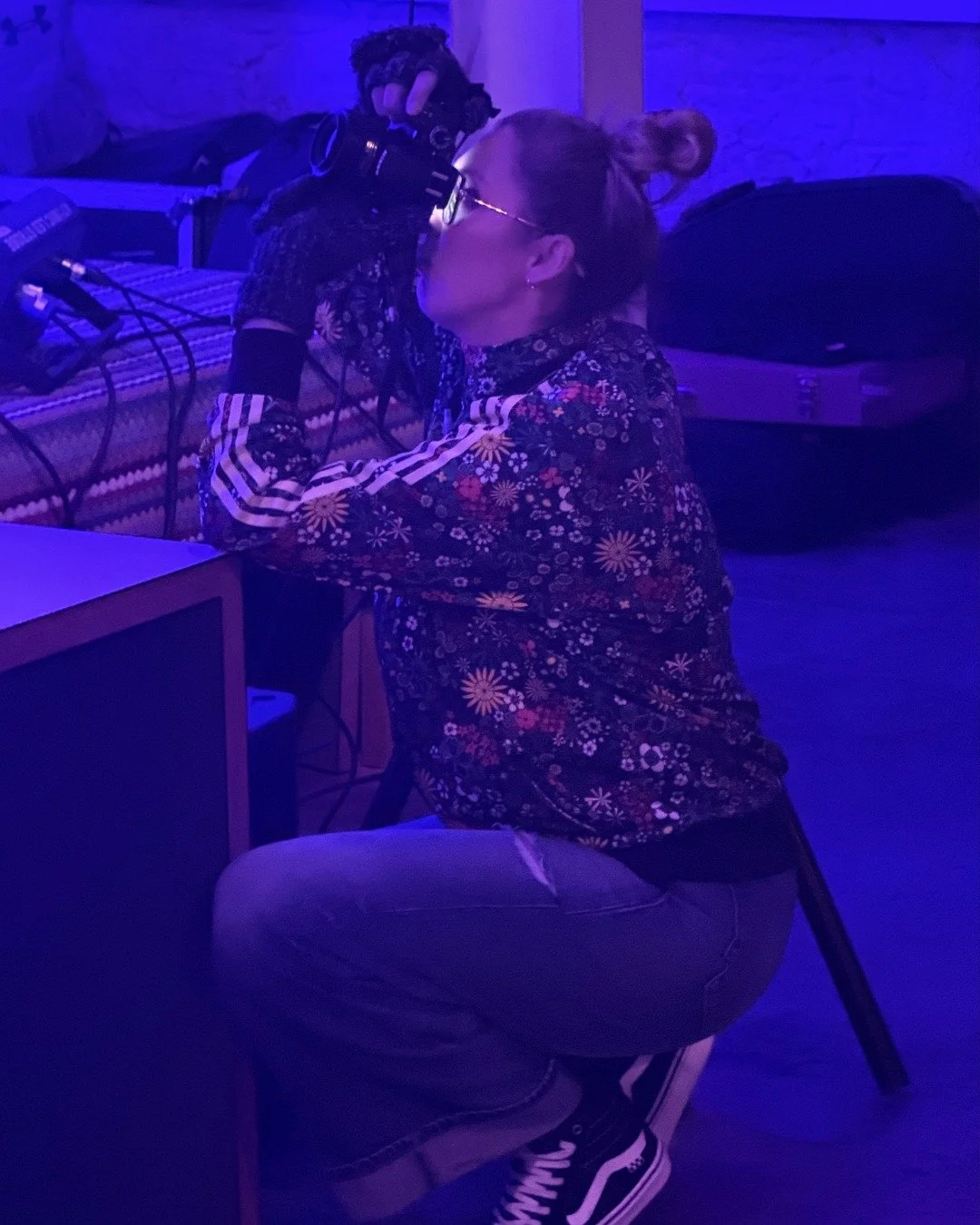 Julia photographing a live performance at Café Momus, Plymouth, kneeling with camera and tripod under purple stage lighting.