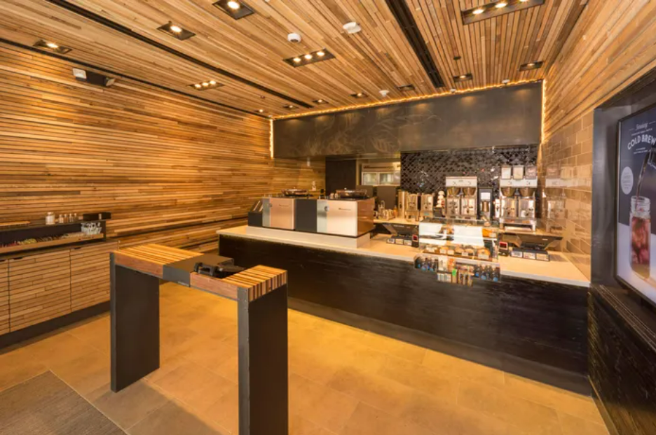 A modern coffee counter with cappuccino machines, a wooden wall, and a digital menu display in a contemporary cafe.
