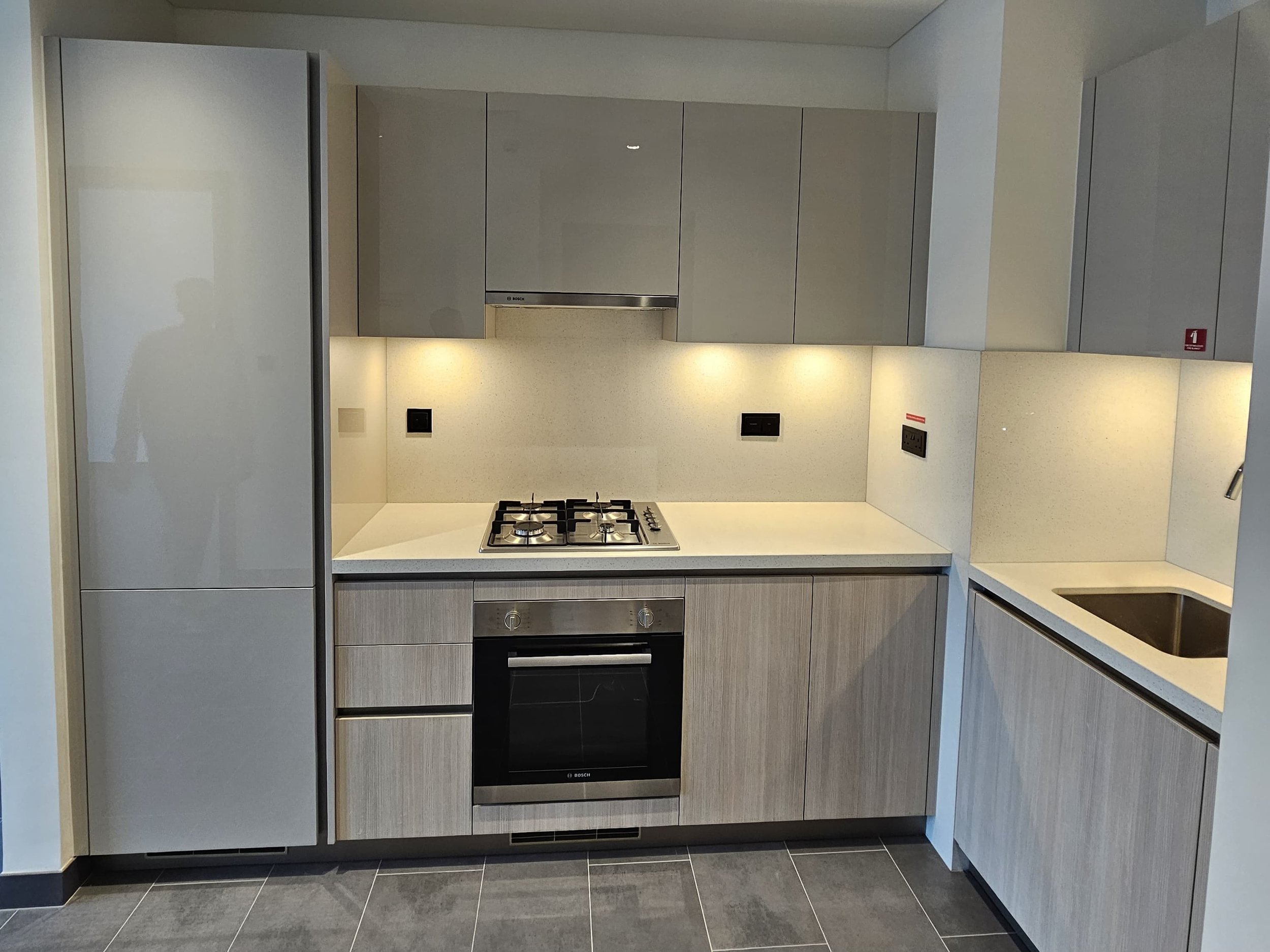 Modern kitchen with gray cabinets, a built-in oven, a gas stove, and a small sink, with black wall outlets and under-cabinet lighting.