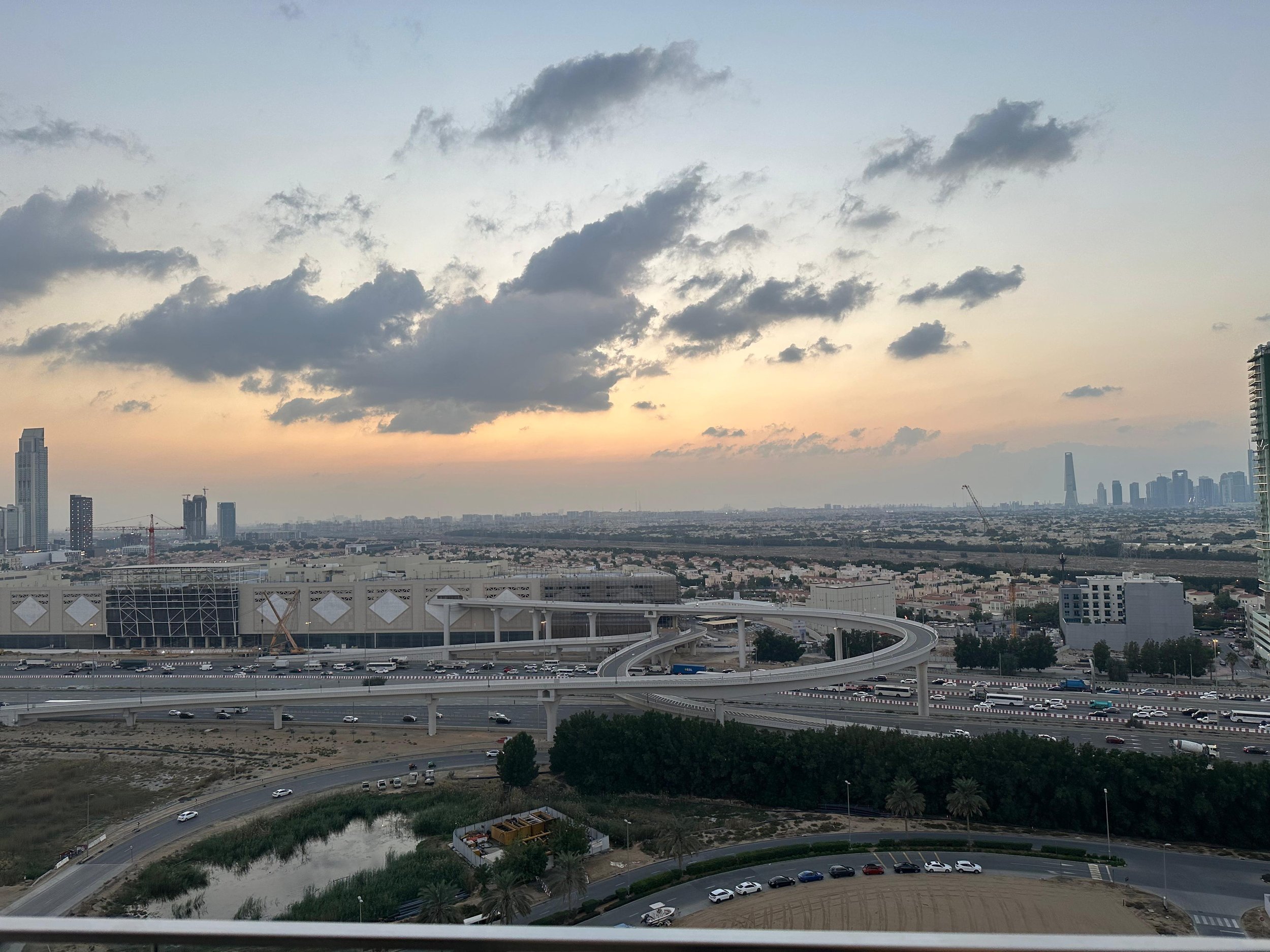 Cityscape view at sunset showing highways, modern buildings, and a cloudy sky.