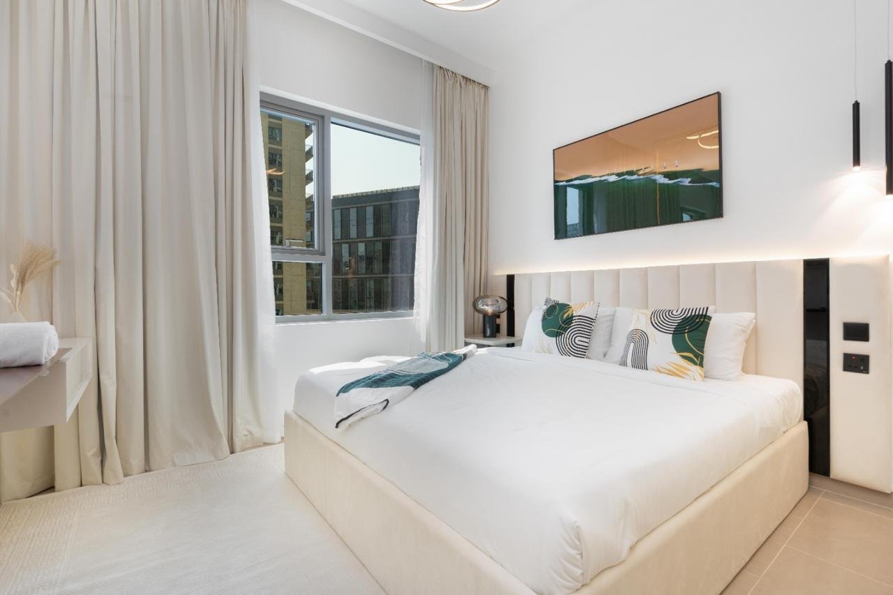 Modern bedroom with white bed, decorative pillows, and a large window with white curtains.