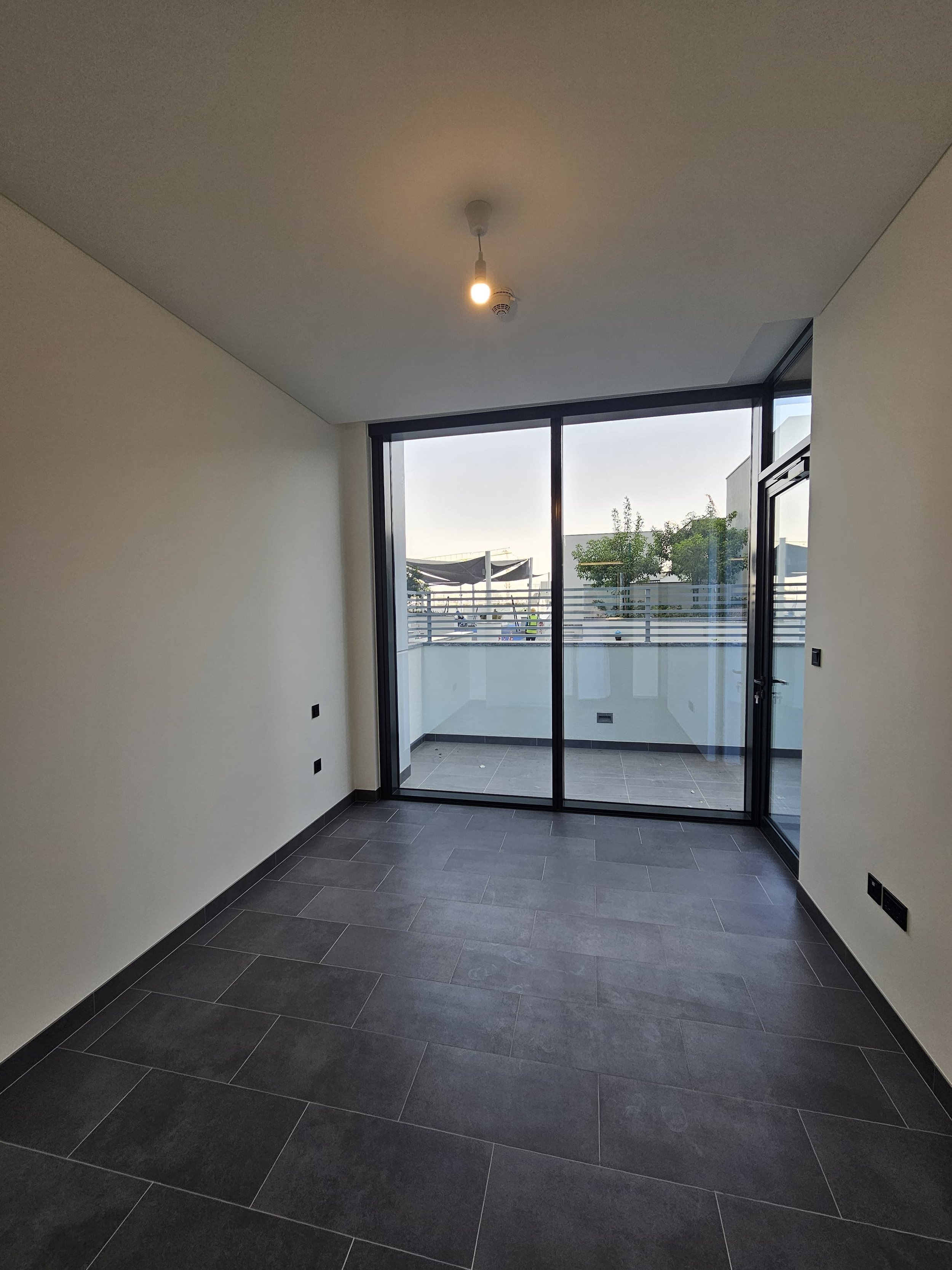 Empty room with large glass sliding door leading to a balcony, dark tiled floor, and white walls.