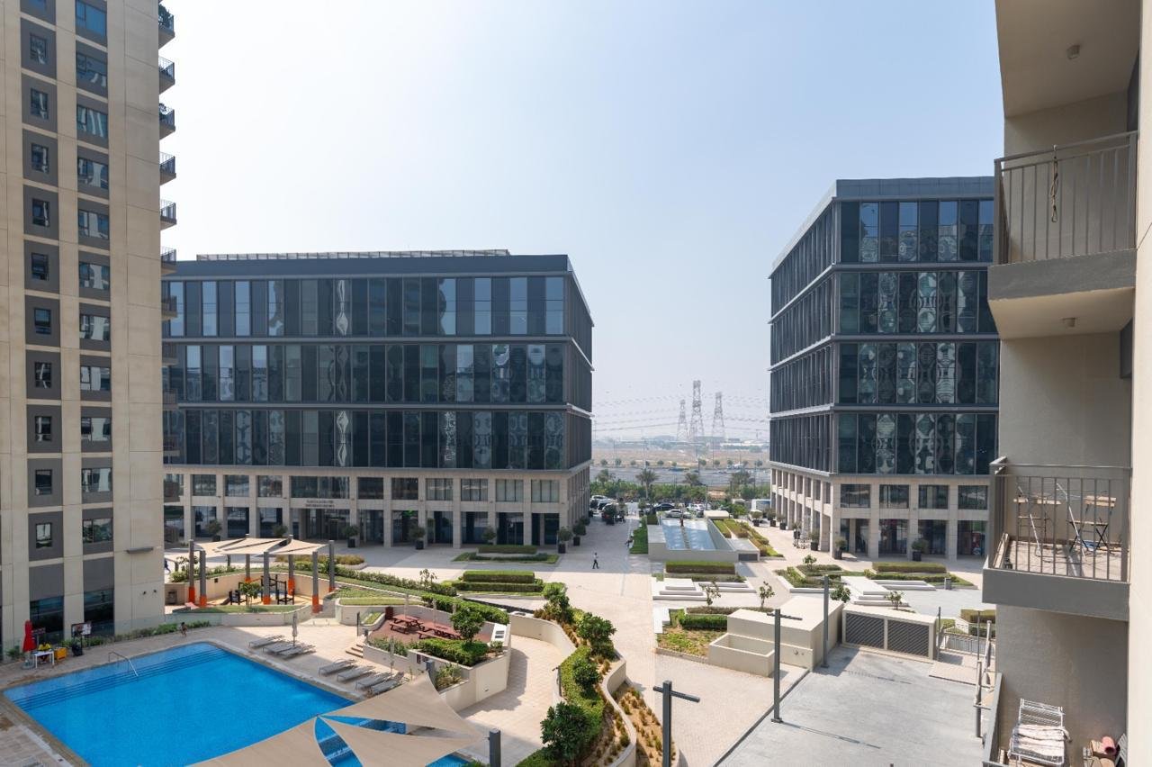 View of a modern apartment complex with glass buildings, a swimming pool, and landscaped outdoor area during daytime.