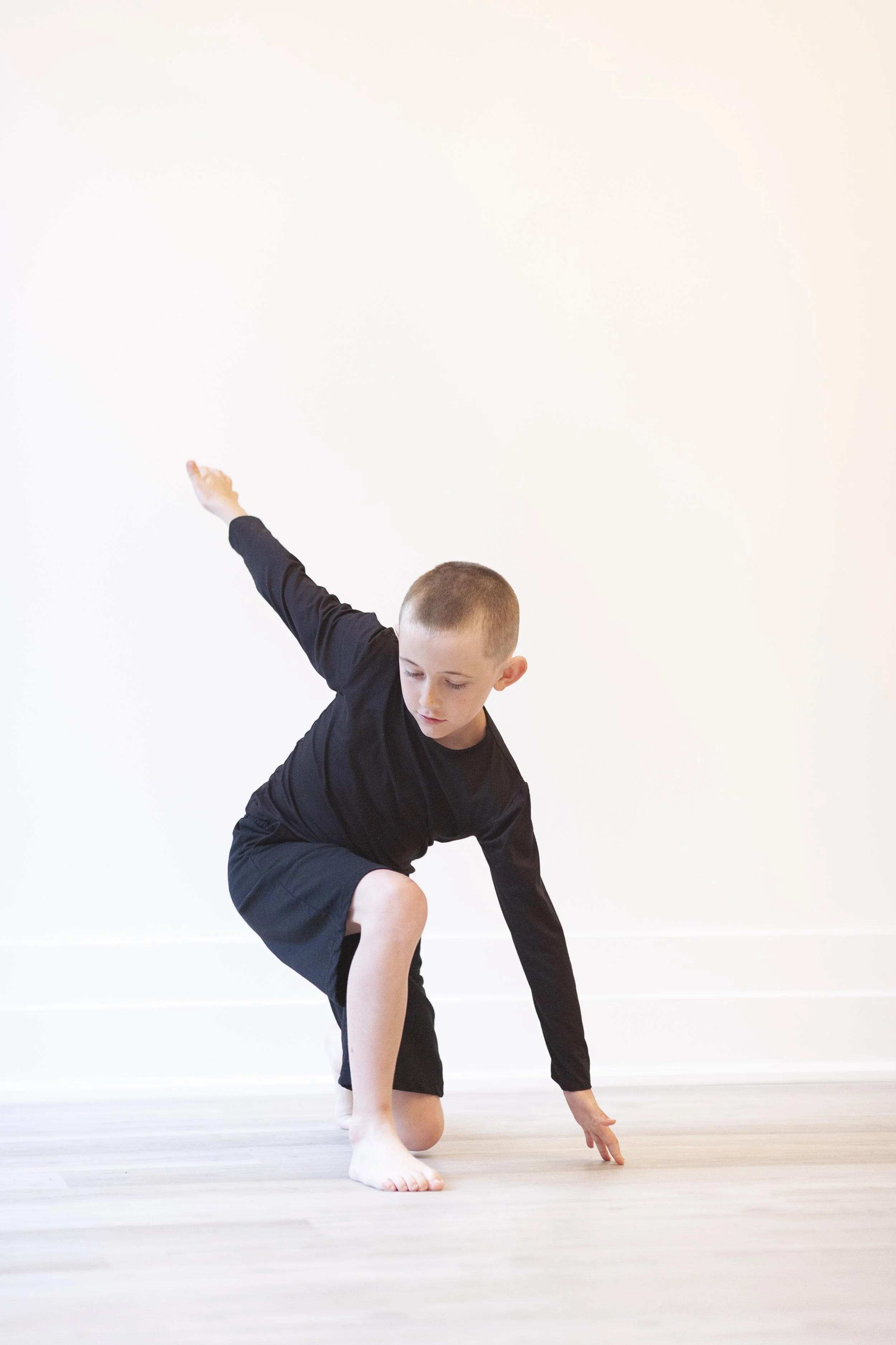 Young boy practicing dance on a wooden floor in a room with plain white walls.