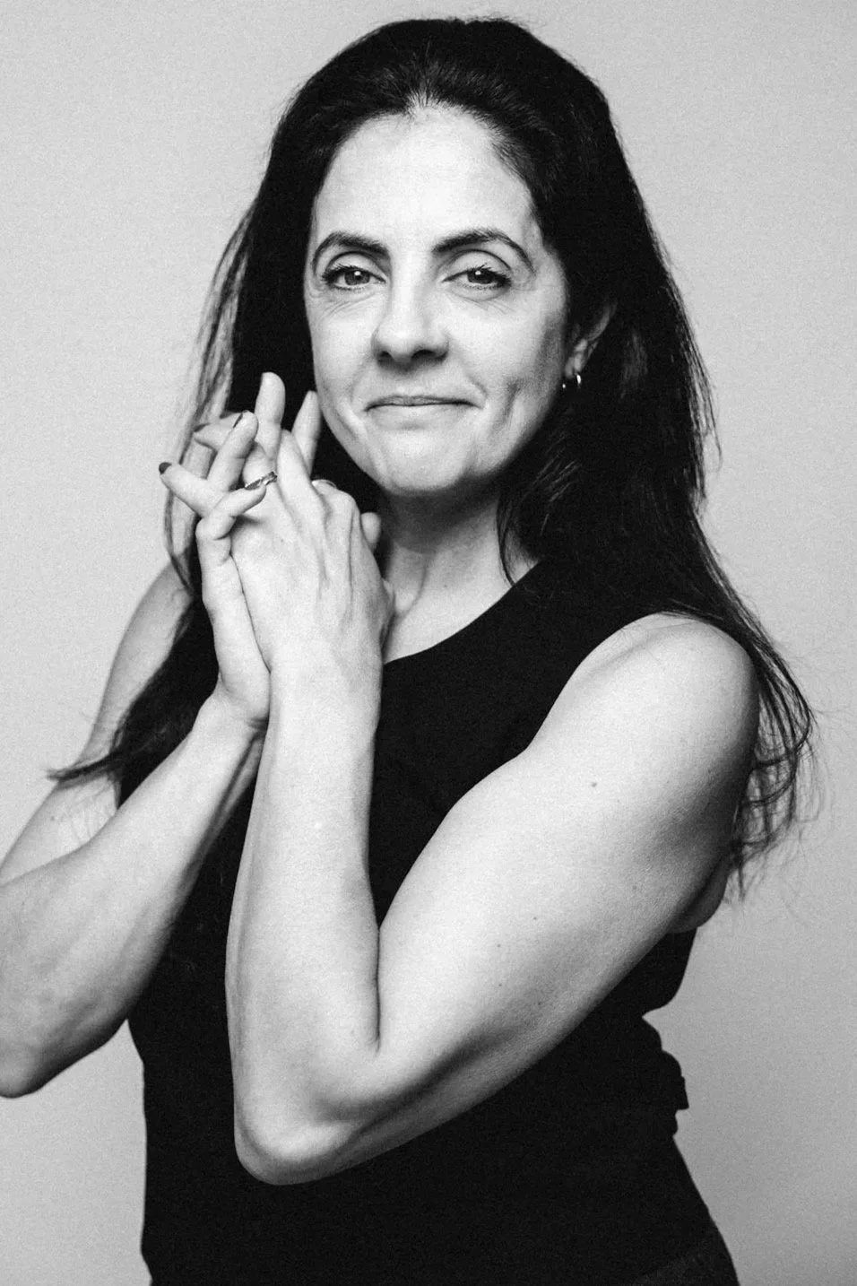 Black and white portrait of a smiling woman with long dark hair, wearing a sleeveless top, looking to her right against a plain background.