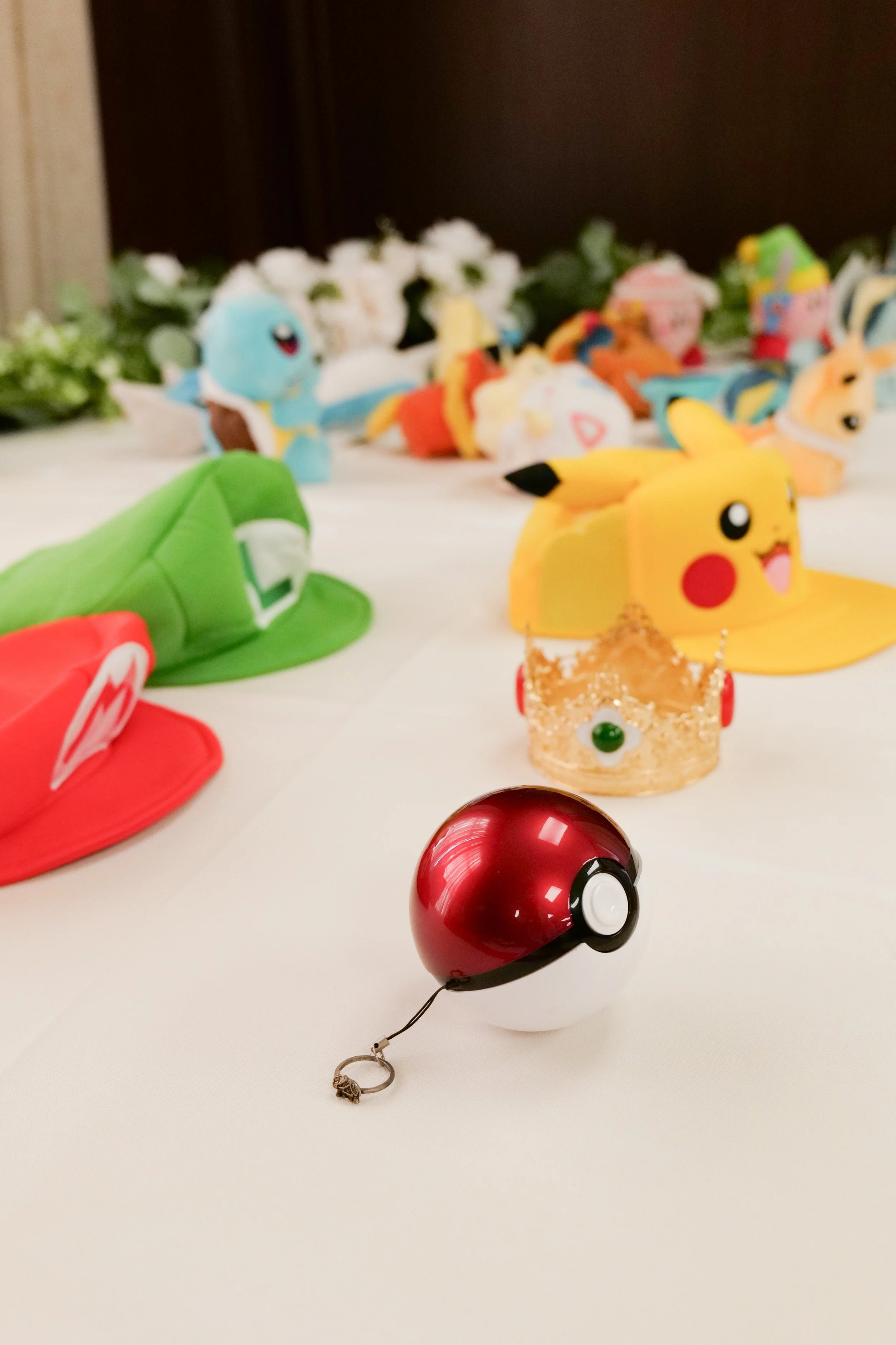 Collection of Pokémon toys and merchandise, including Pikachu, Poké Balls, and characters, displayed on a white surface with floral decorations in the background.