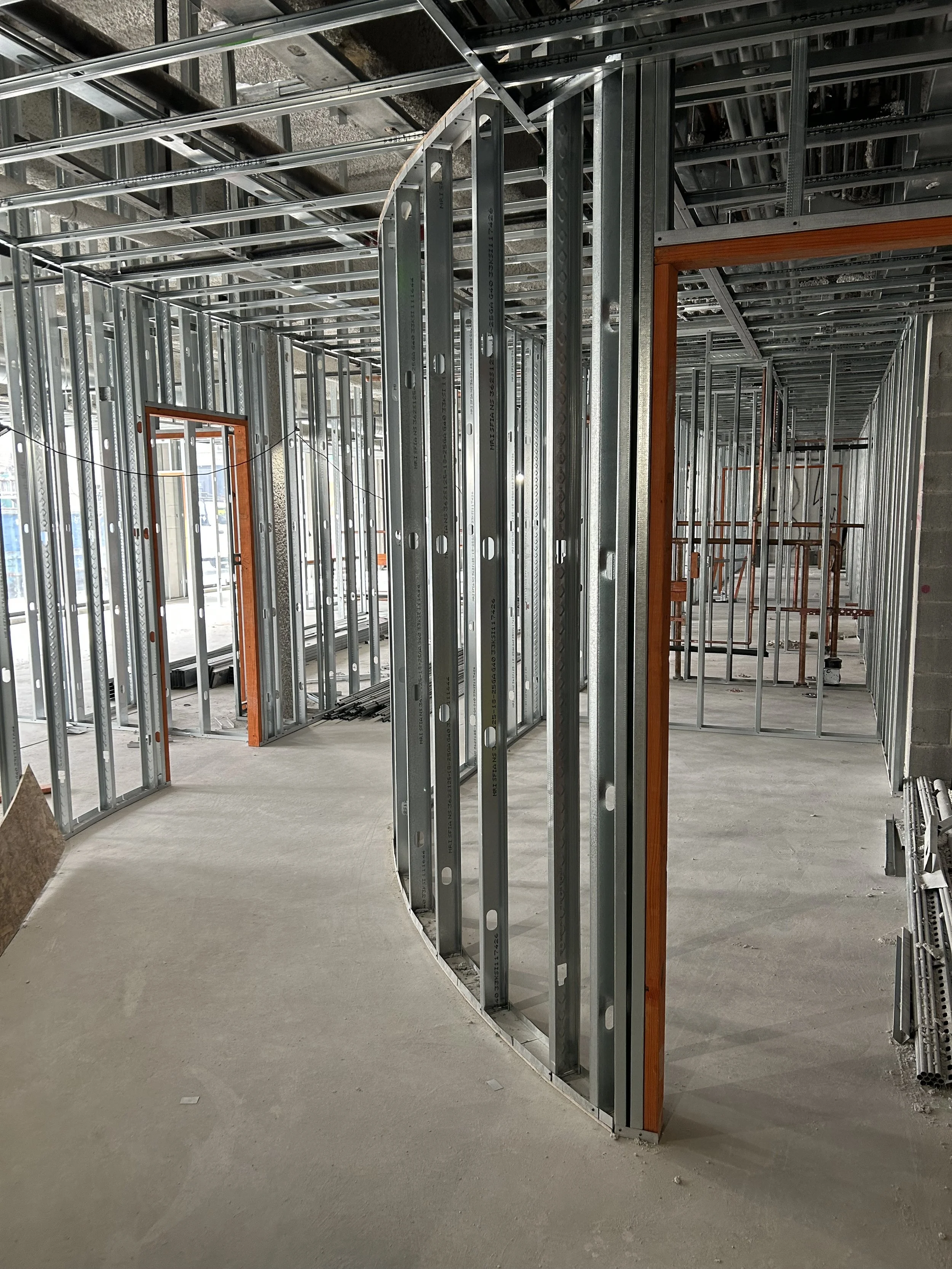 Interior view of a building under construction, showing metal framing, door openings, and a curved concrete floor.