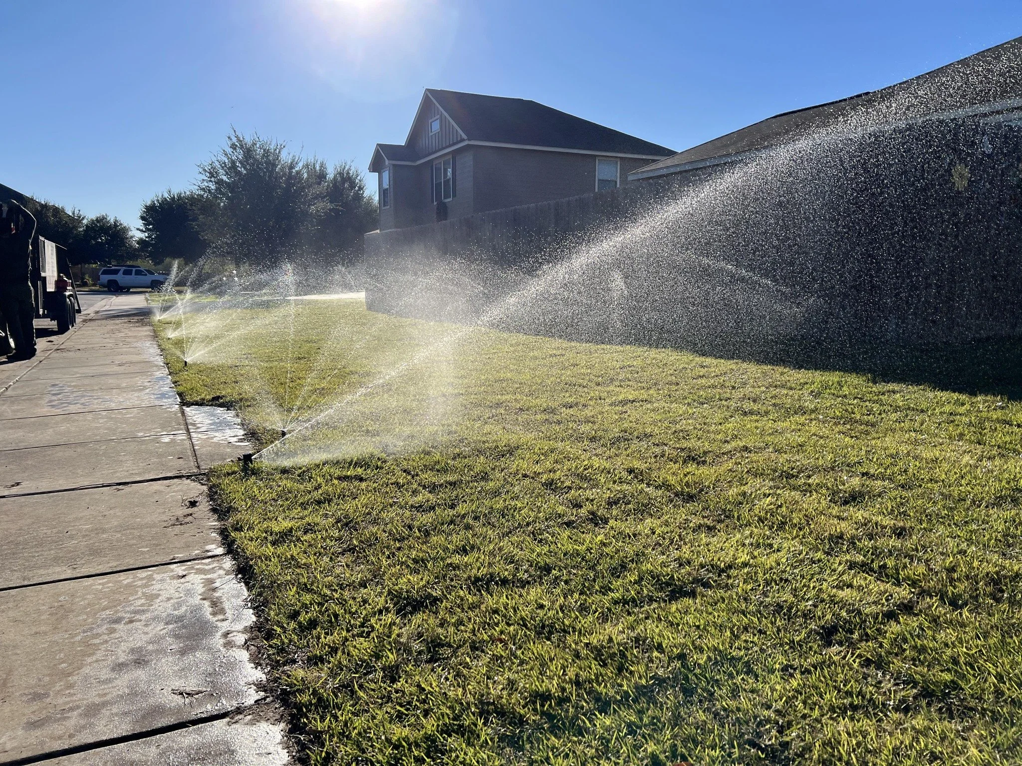Sprinklers watering a front lawn in front of a house on a sunny day.