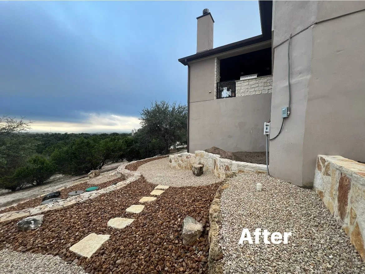 Landscaped backyard with gravel path leading to house, new stone border, and a scenic view of trees and cloudy sky in the background.