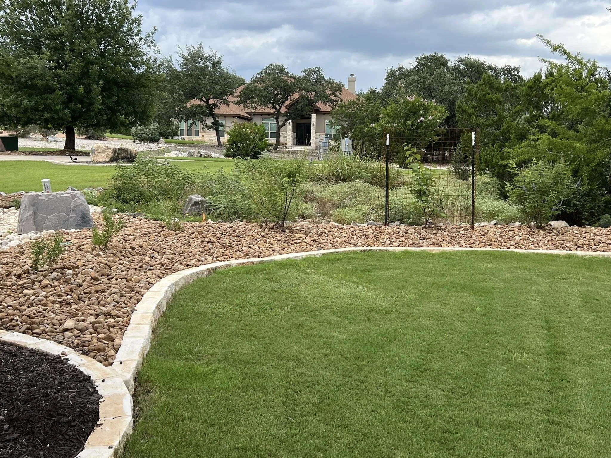 Lawn with curved stone border, green grass, and a landscaped area with rocks and plants in a residential yard