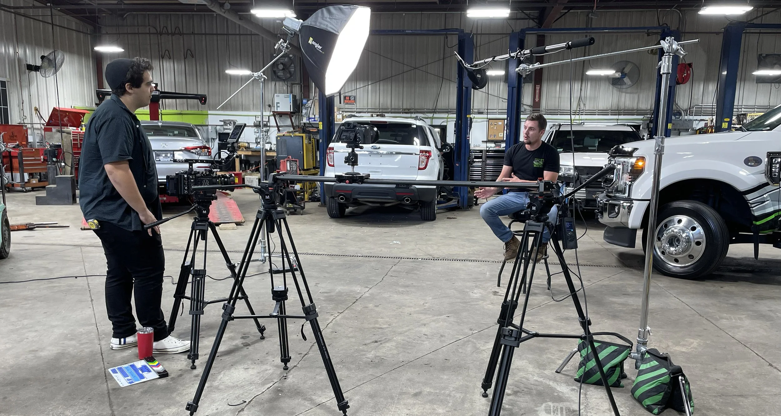 Benjamin DosSantos interviewing a client on set for a commercial video shoot, with lights, cameras, and production equipment in view.