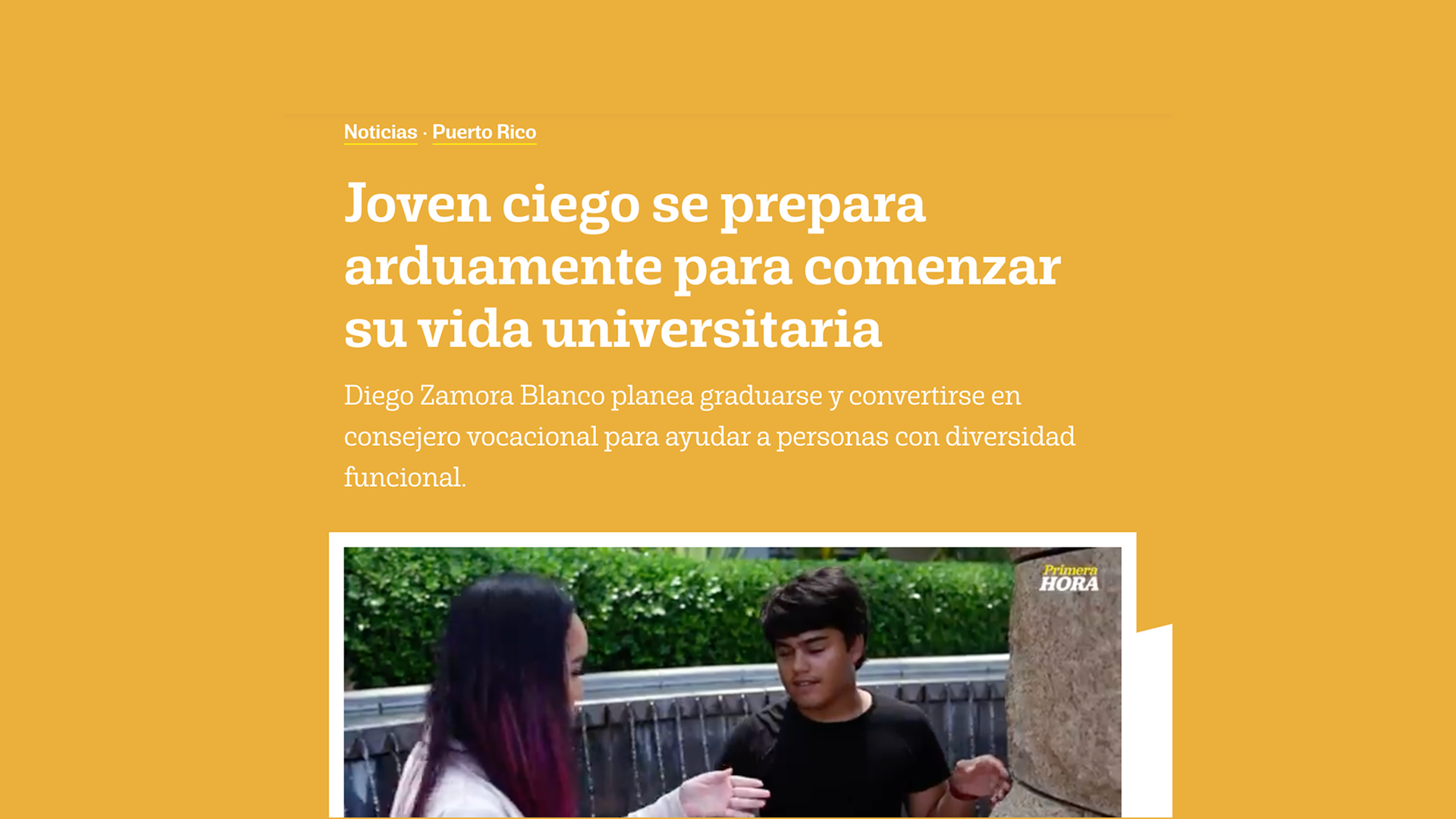 Diego Zamora Blanco camina con su bastón blanco junto a Jey, quien lo acompaña mientras pasan frente a una fuente rodeada de vegetación.