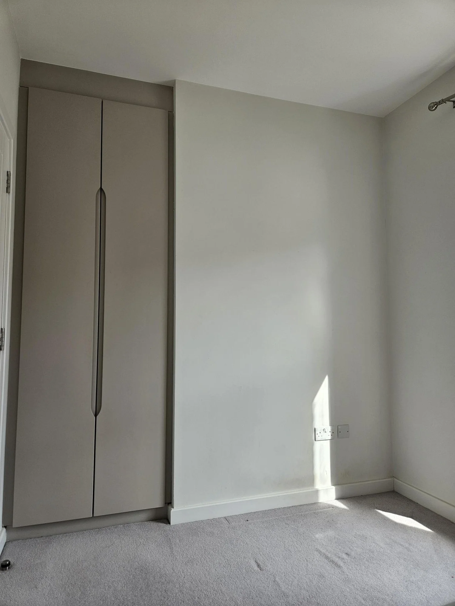 Empty corner of a room with a wardrobe and electrical outlets on the wall.