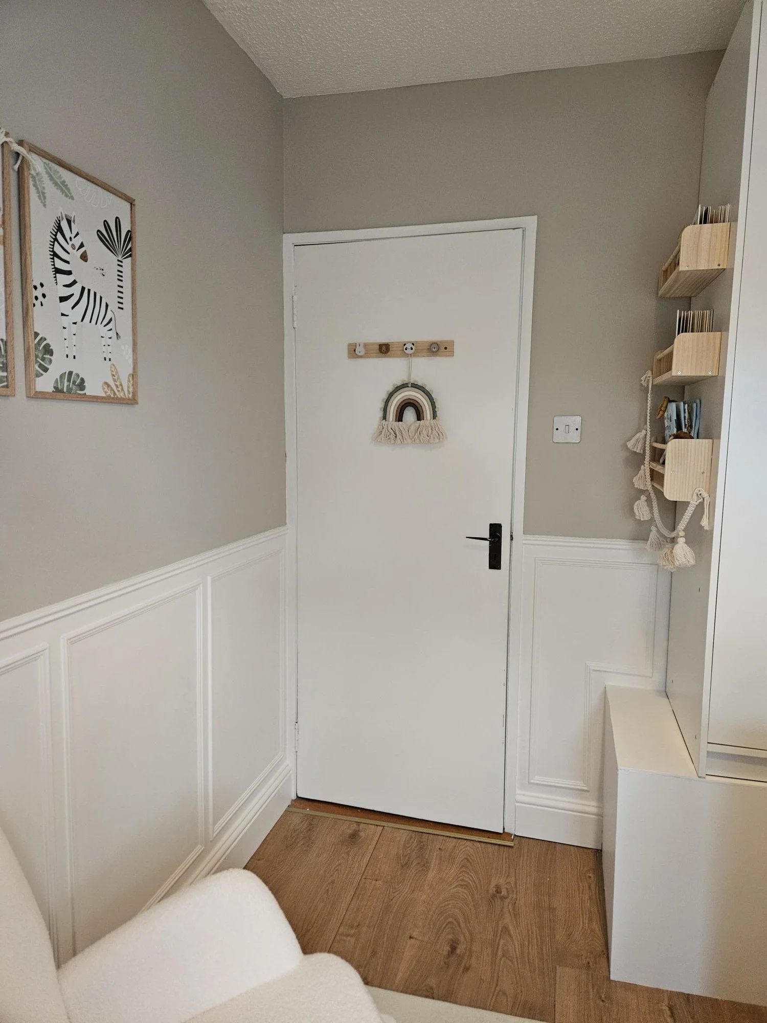 Interior view of a room doorway decorated with children's wall art and hanging decor, with wood flooring and beige walls. By KF Designs