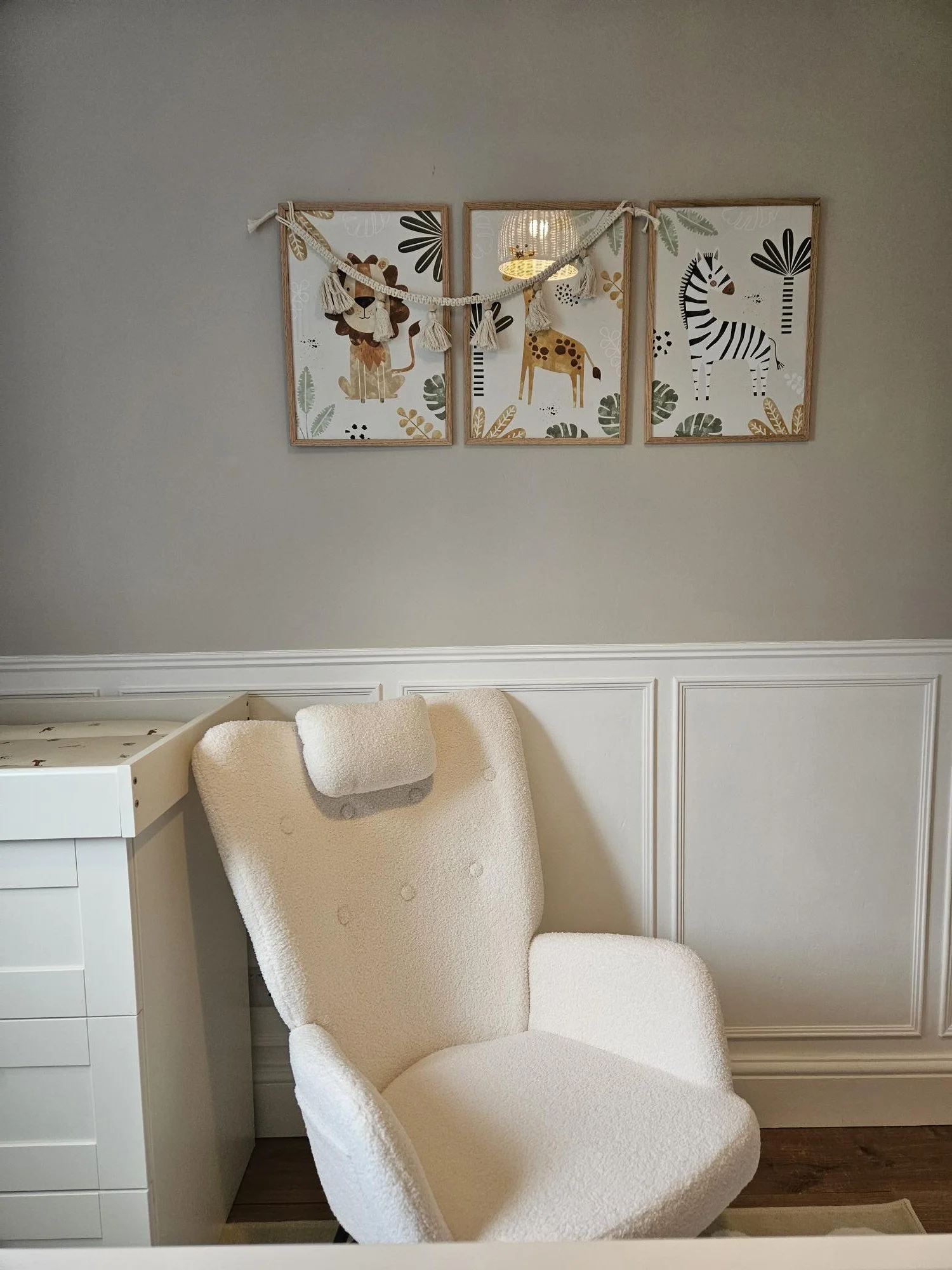 A nursery corner featuring three jungle animal themed art prints on the wall, a white upholstered lounge chair with a matching bolster pillow, and part of a white dresser to the left. By KF Designs