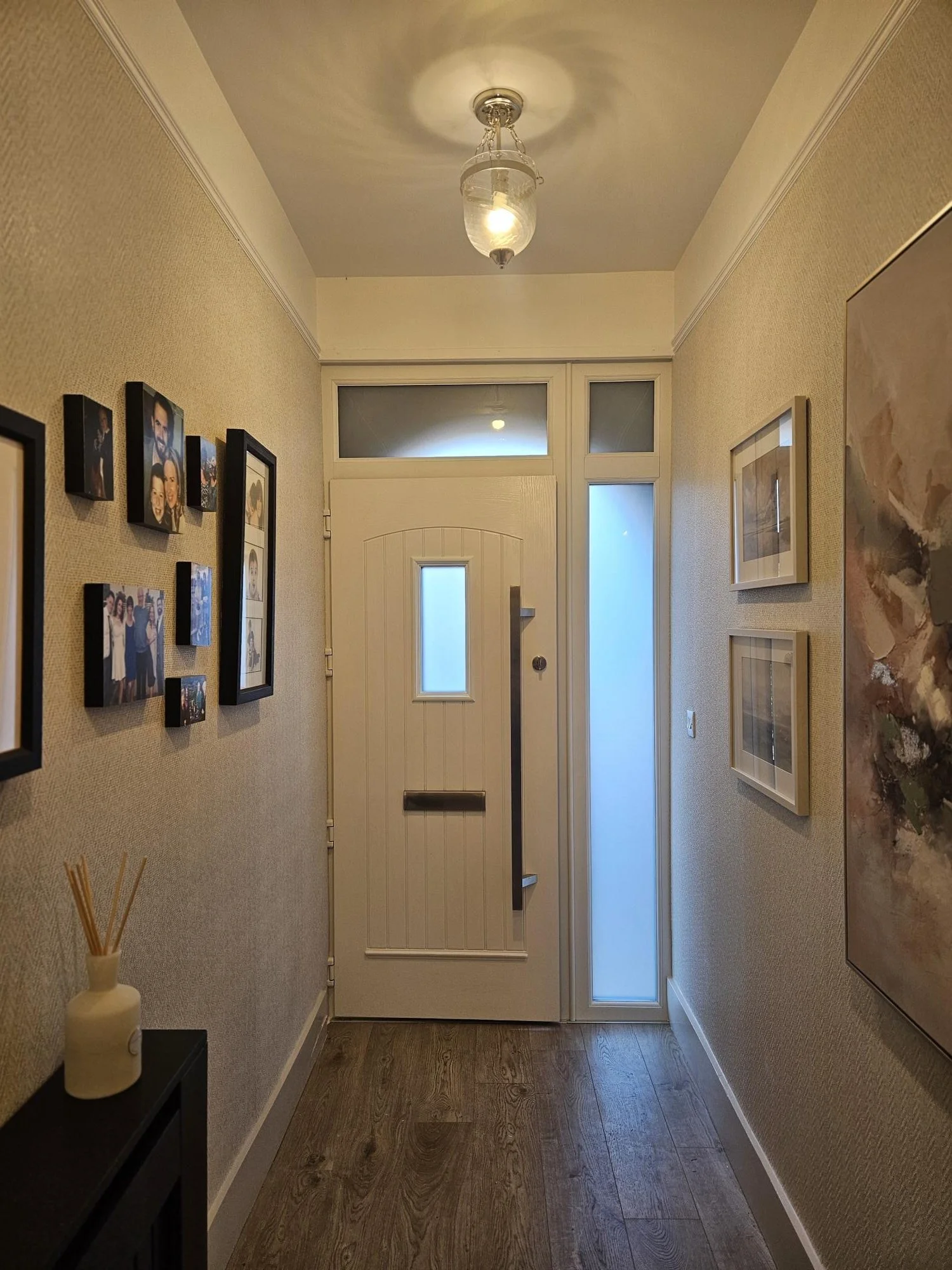 Entryway with a white front door, frosted glass panels, surrounded by artwork and family photos on the walls. By KF Designs