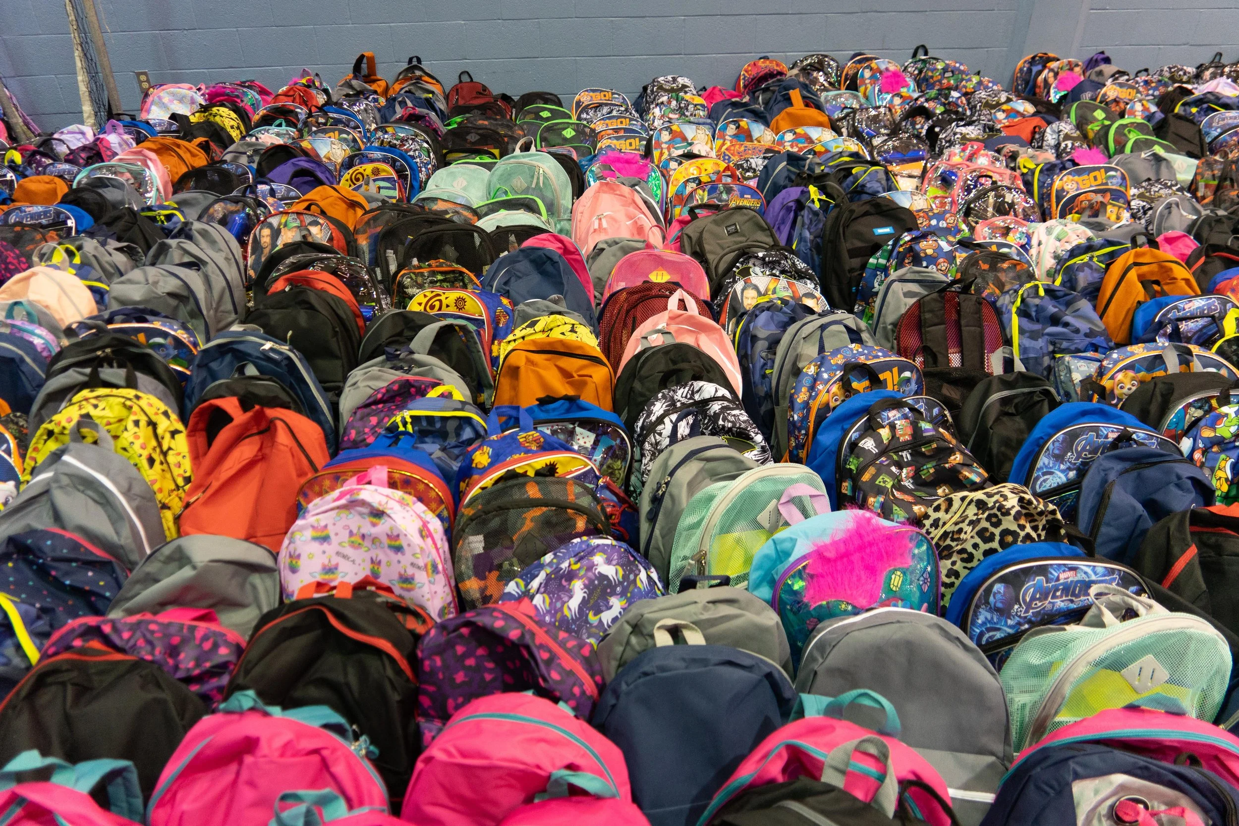 A large collection of colorful backpacks arranged in rows against a blue wall.