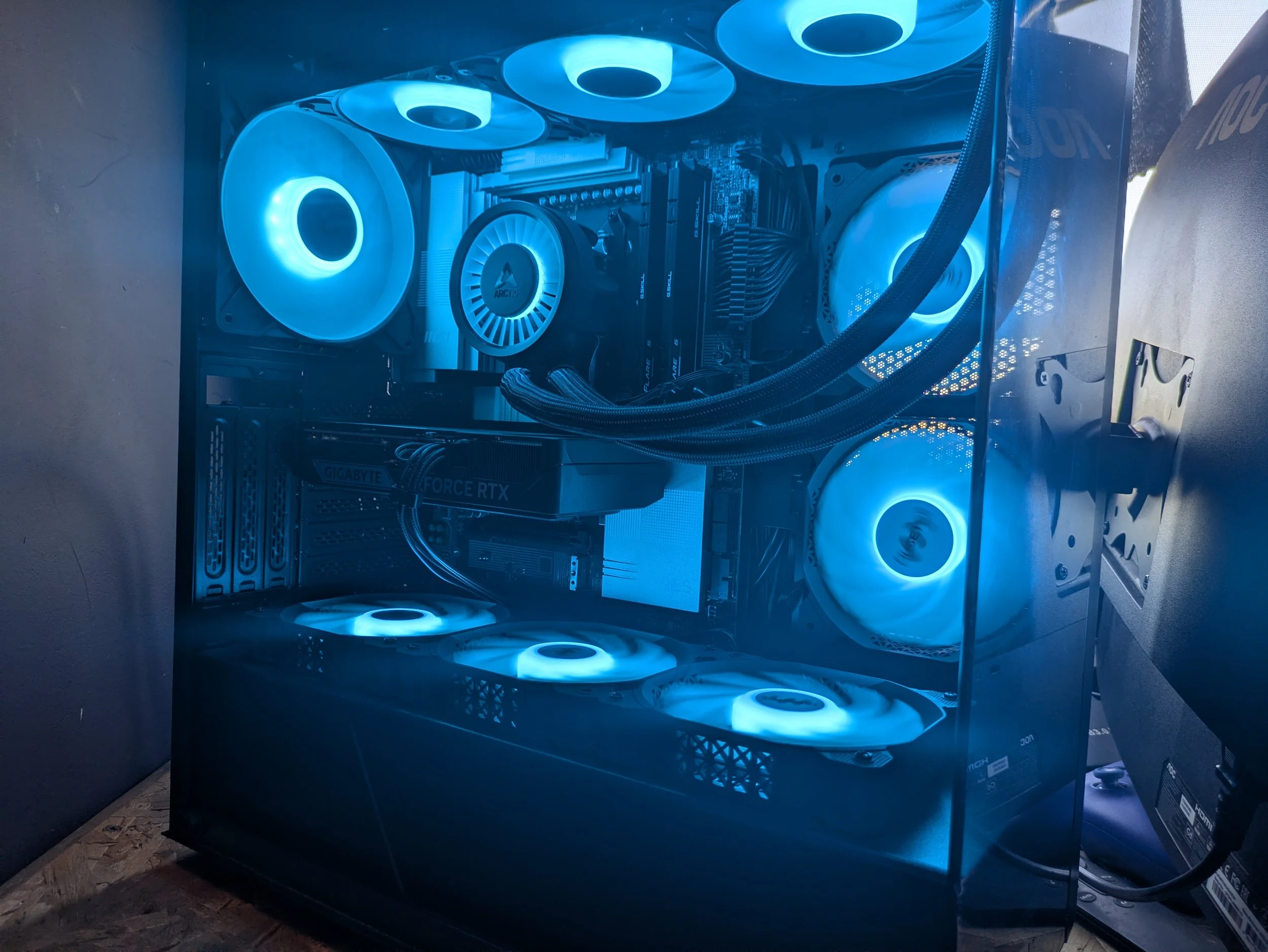 A gaming computer with a transparent side panel, illuminated by blue LED lights, showing internal components including cooling fans, motherboard, graphics card, and power supply.