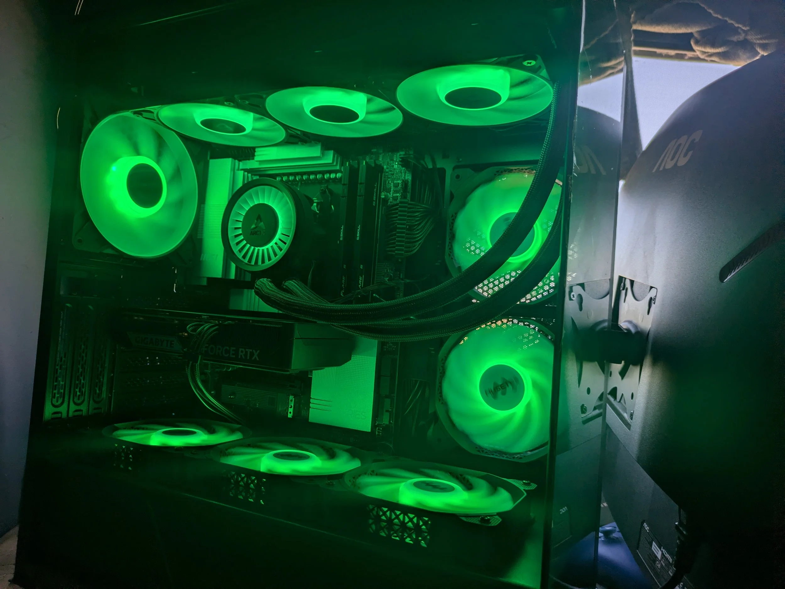 A gaming computer with a transparent side panel, illuminated by green LED lights, showing internal components including cooling fans, motherboard, graphics card, and power supply.