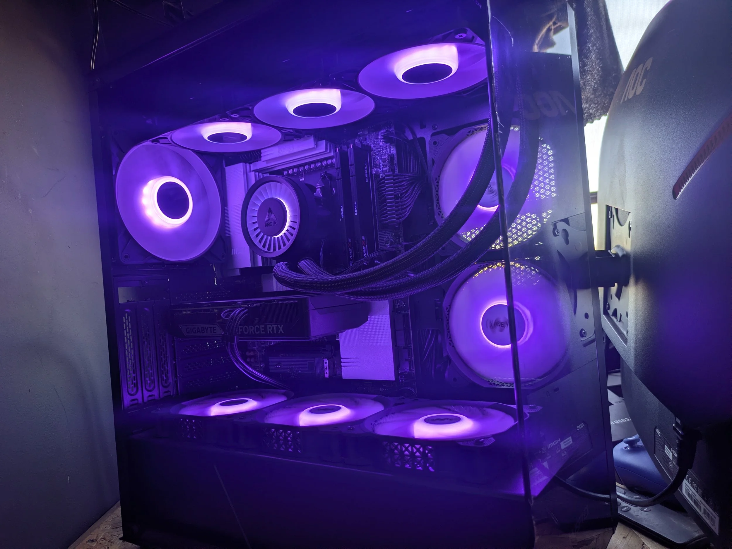 A gaming computer with a transparent side panel, illuminated by purple LED lights, showing internal components including cooling fans, motherboard, graphics card, and power supply.