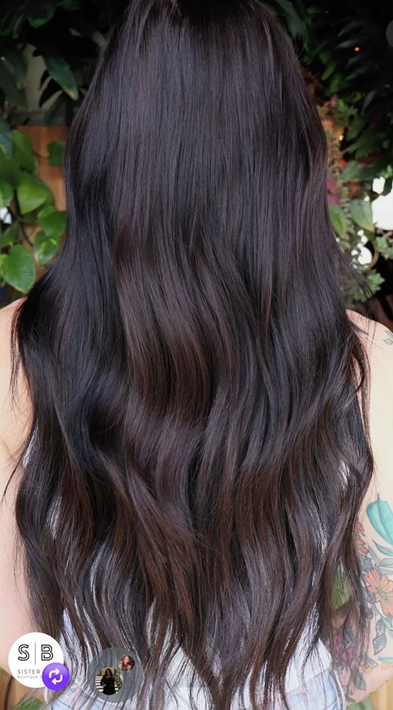 Back view of long, wavy, dark brown or black hair with subtle reddish highlights.