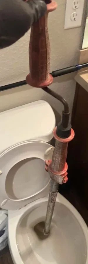 Using a professional-grade closet auger to clear a stubborn toilet blockage in a Jacksonville residential bathroom.