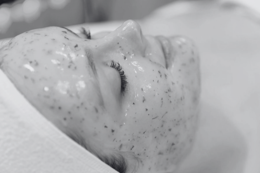 Close-up of a person's face with a speckled facial mask, lying down with eyes closed.