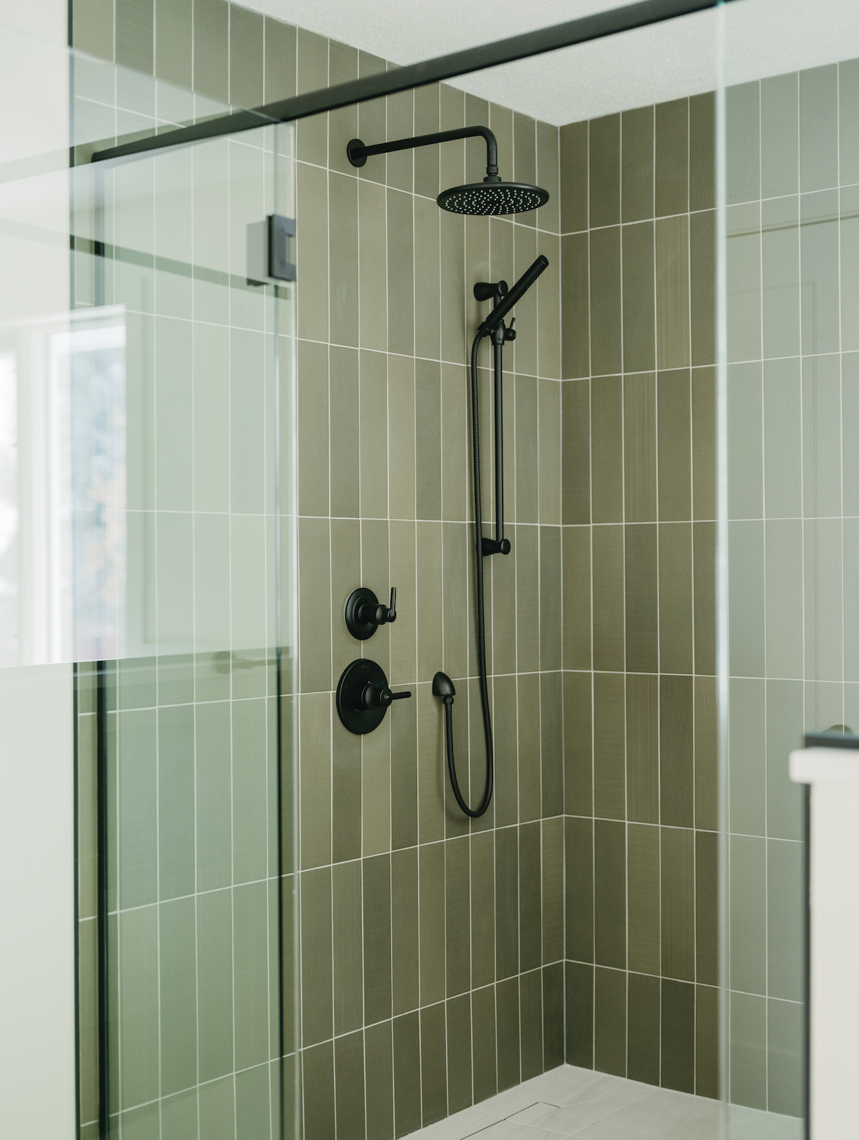 Shower area with green tiles, black showerhead, handheld shower attachment, and glass enclosure.