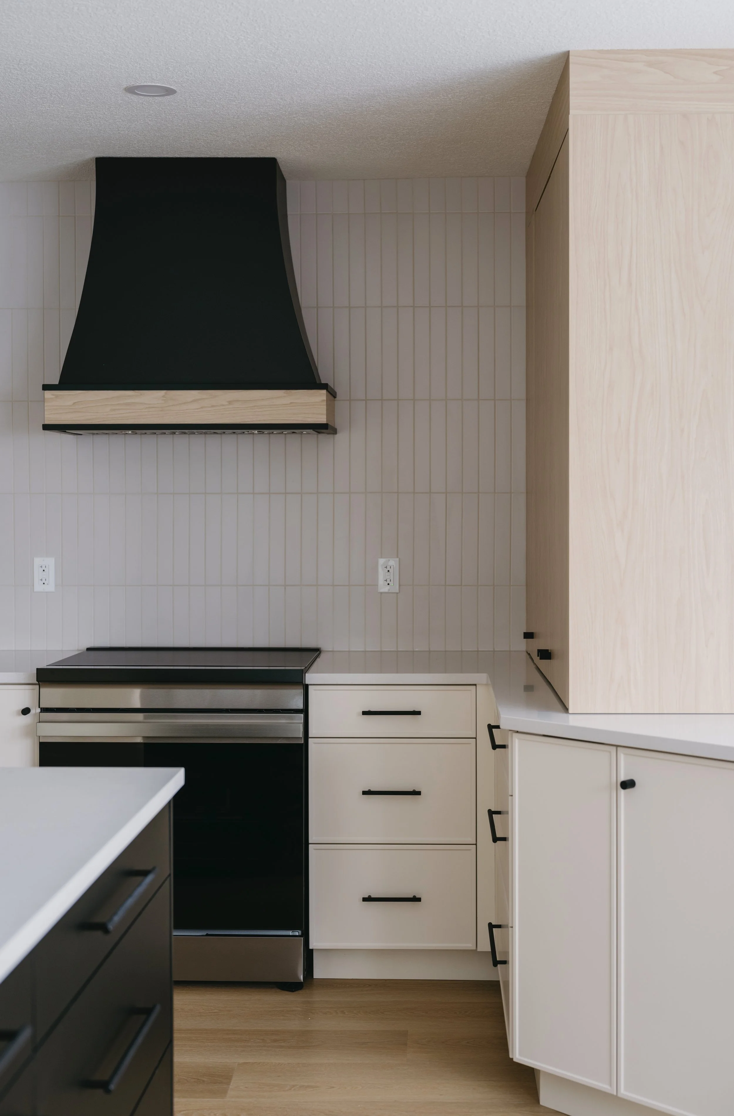 Modern kitchen with beige and black cabinetry, a black stove, a black and wood range hood, and a wood floor.