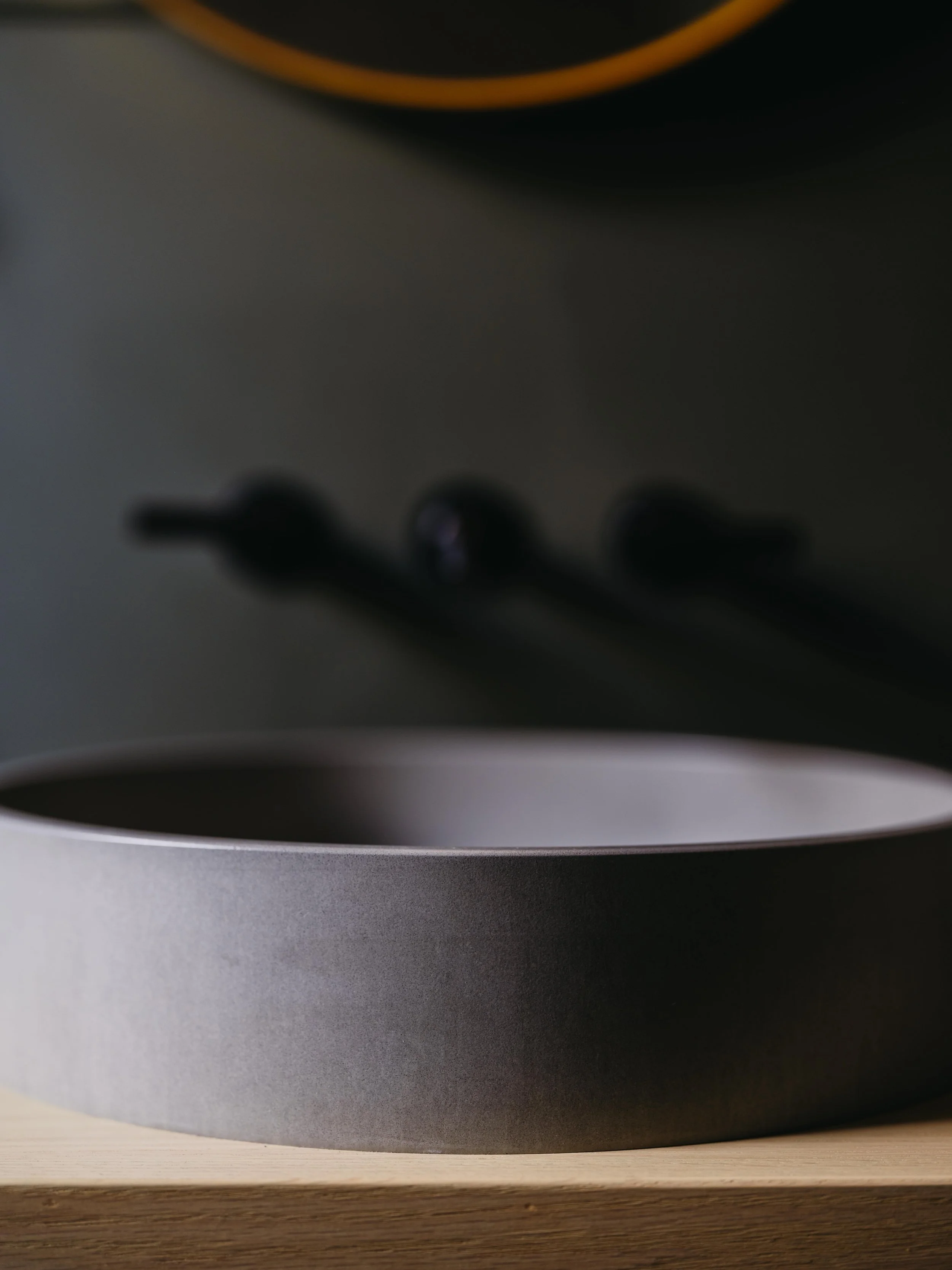 Close-up of a custom powder room renovation. With a concrete sink, moody green walls, wood vanity, kohler wall-mounted faucet