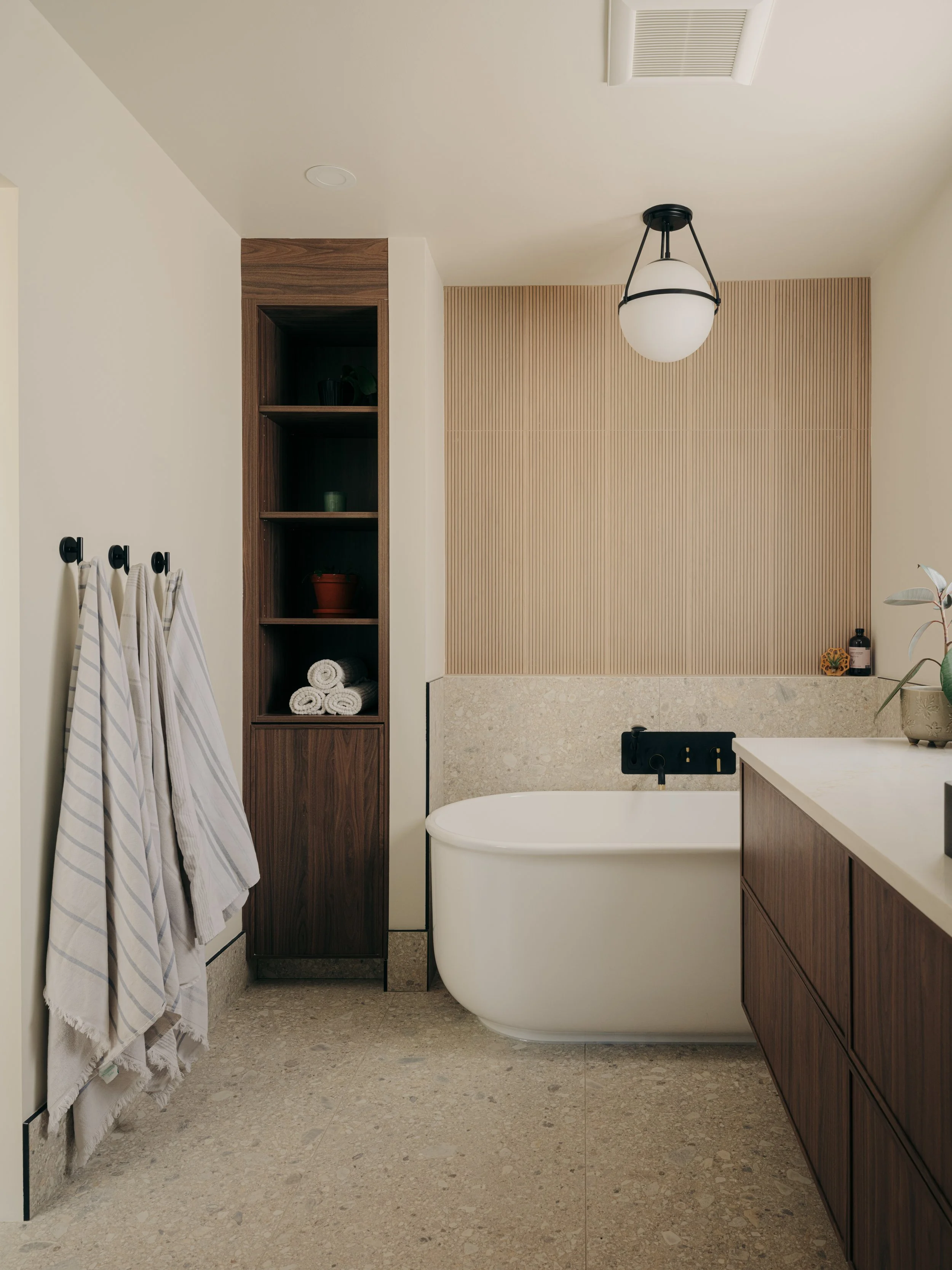 Modern bathroom with a freestanding bathtub, wooden cabinetry, and a textured beige wall panel.