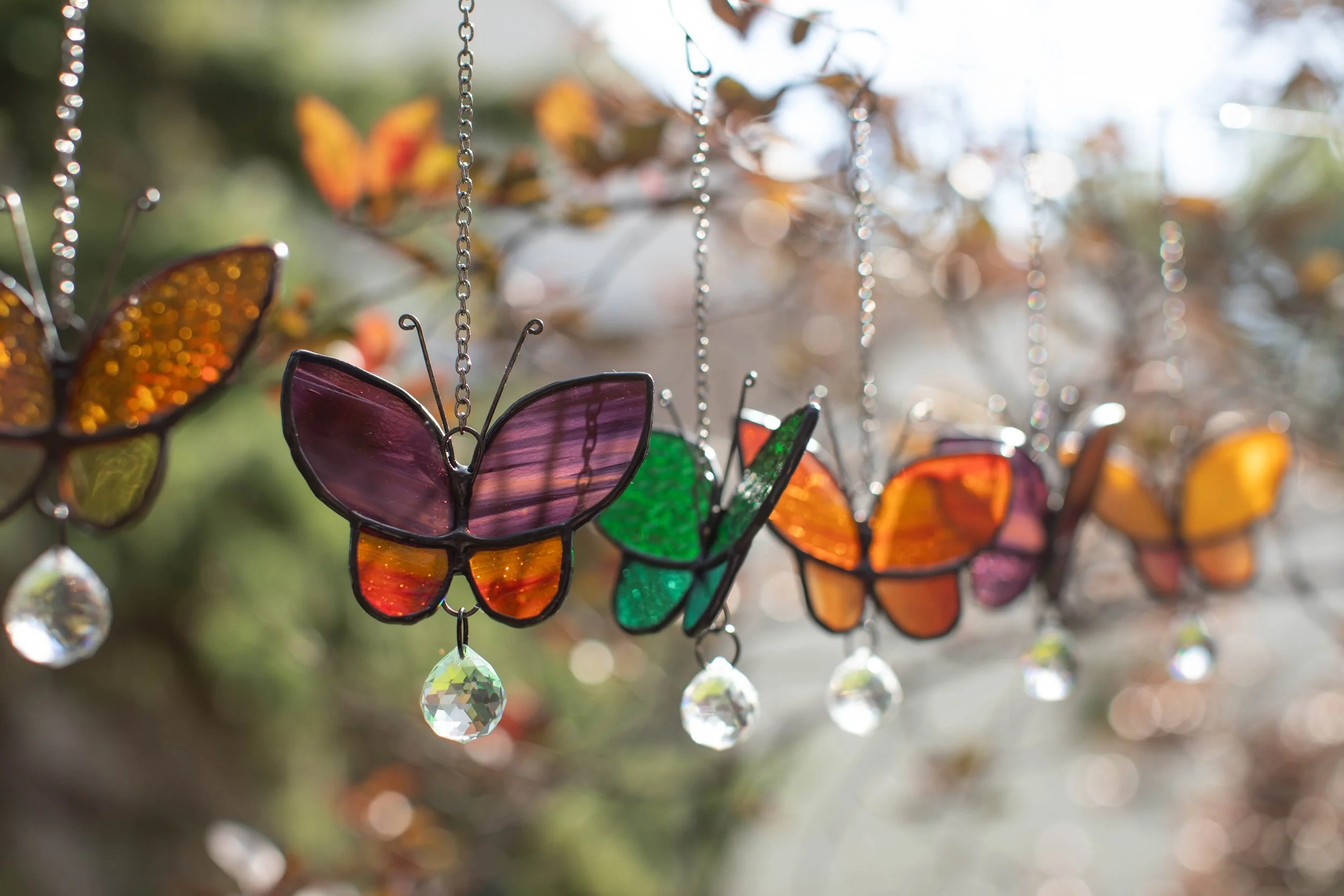 Colorful butterfly-shaped stained glass hanging ornaments with crystal drops in sunlight.