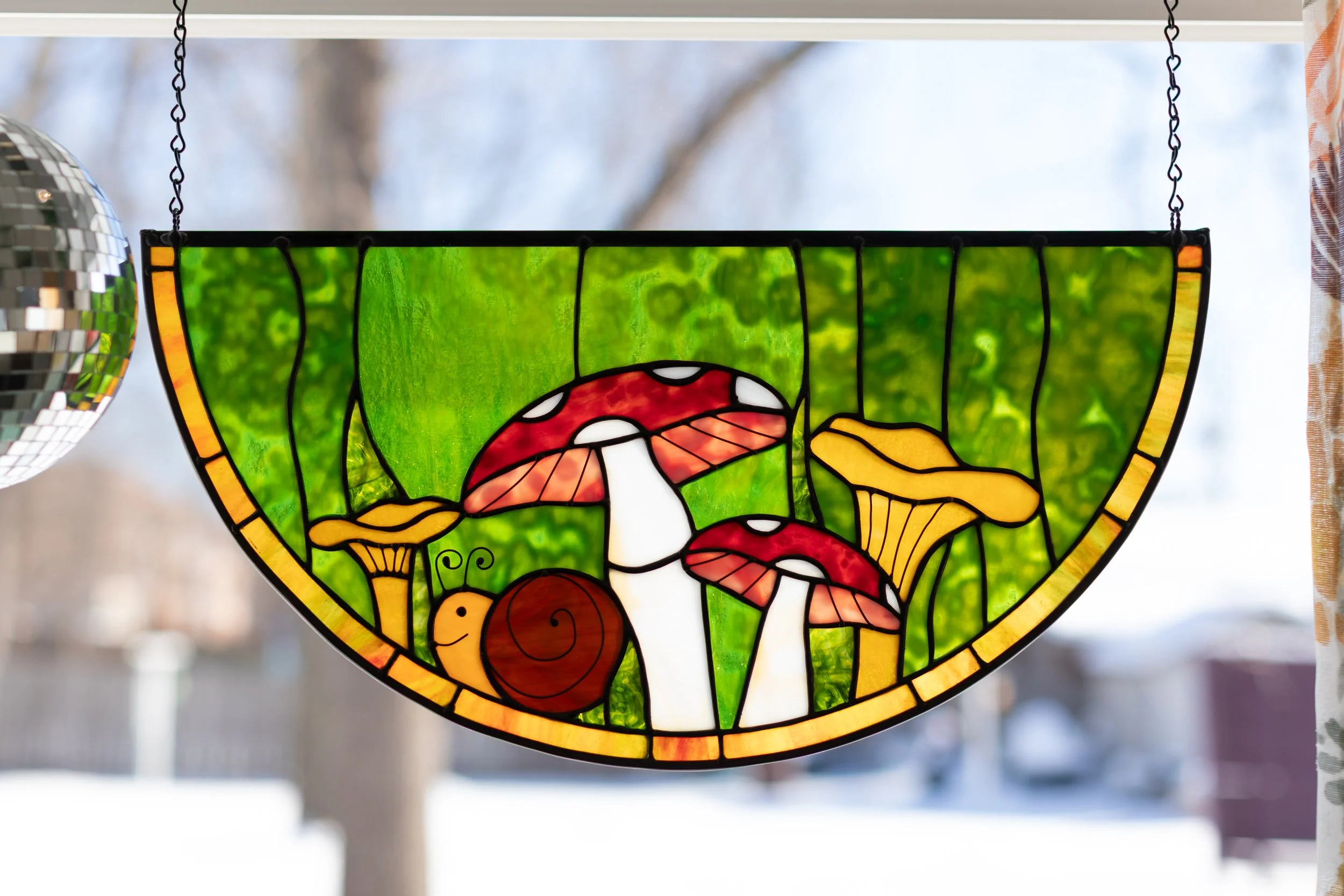 Stained glass window depicting a whimsical scene of woodland mushrooms, a snail, and green foliage.