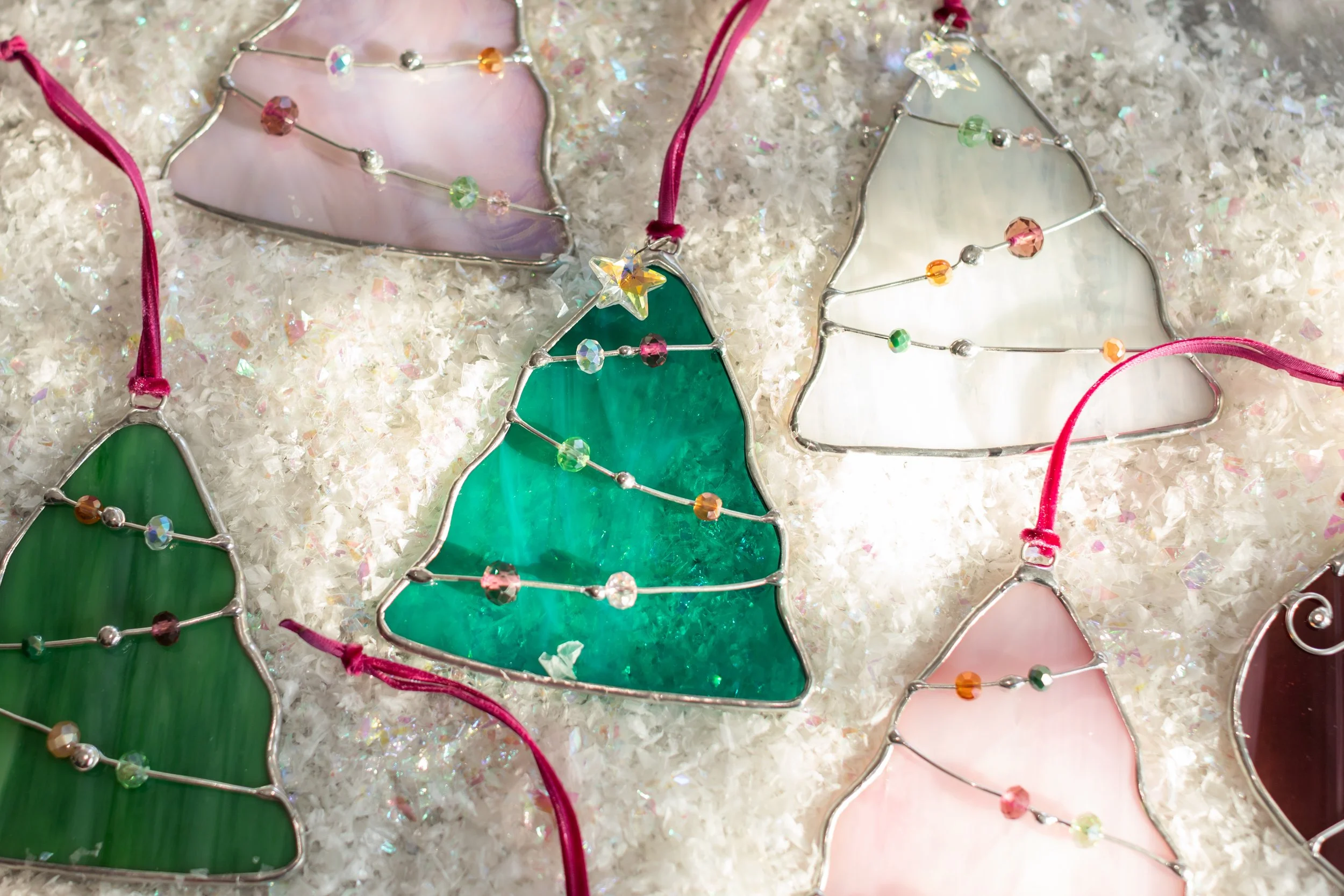 Colorful stained glass Christmas tree ornaments with beaded wire decoration, laid on artificial snow.