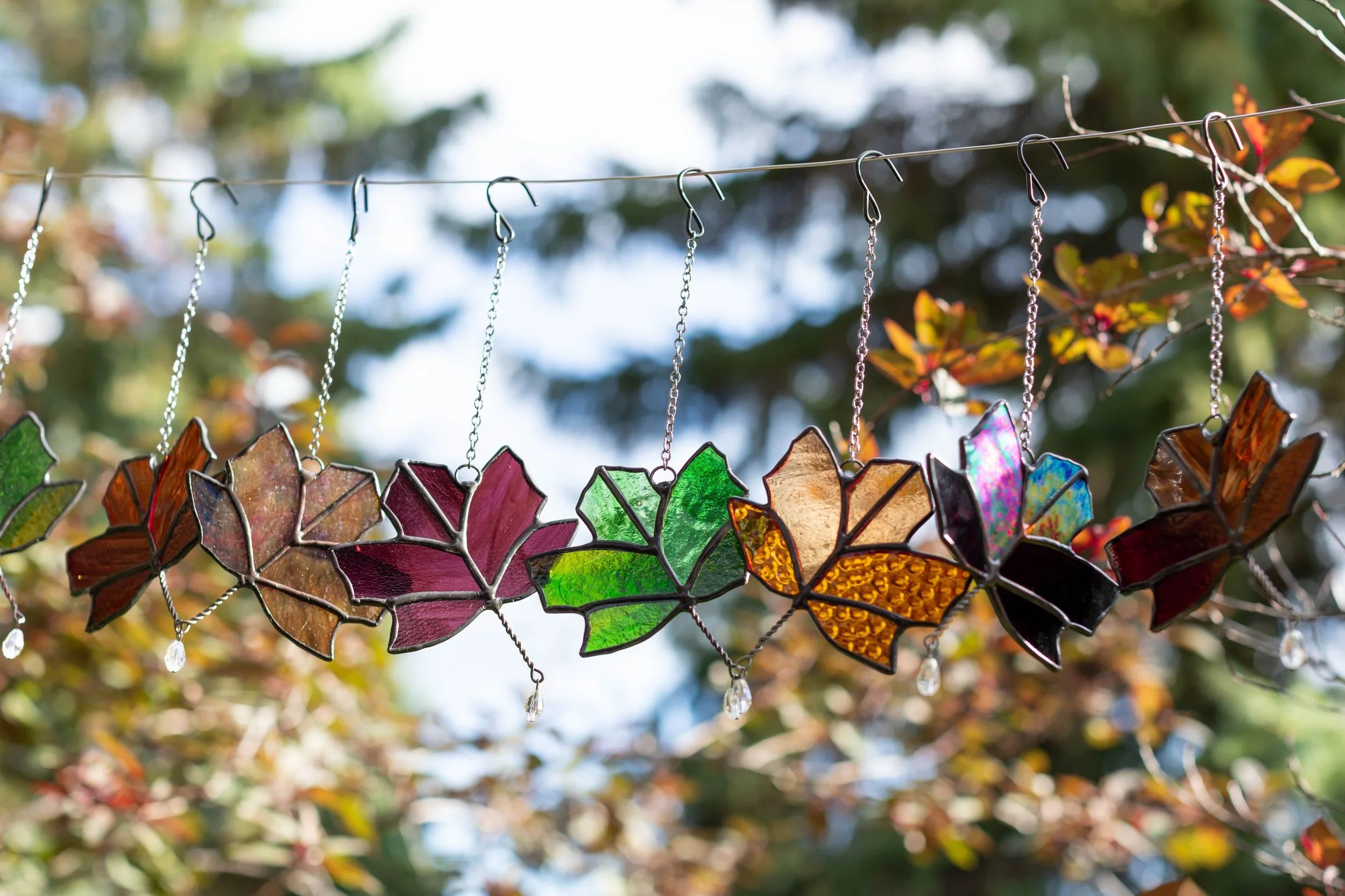 Colorful stained glass leaf ornaments hanging from a wire outdoors.