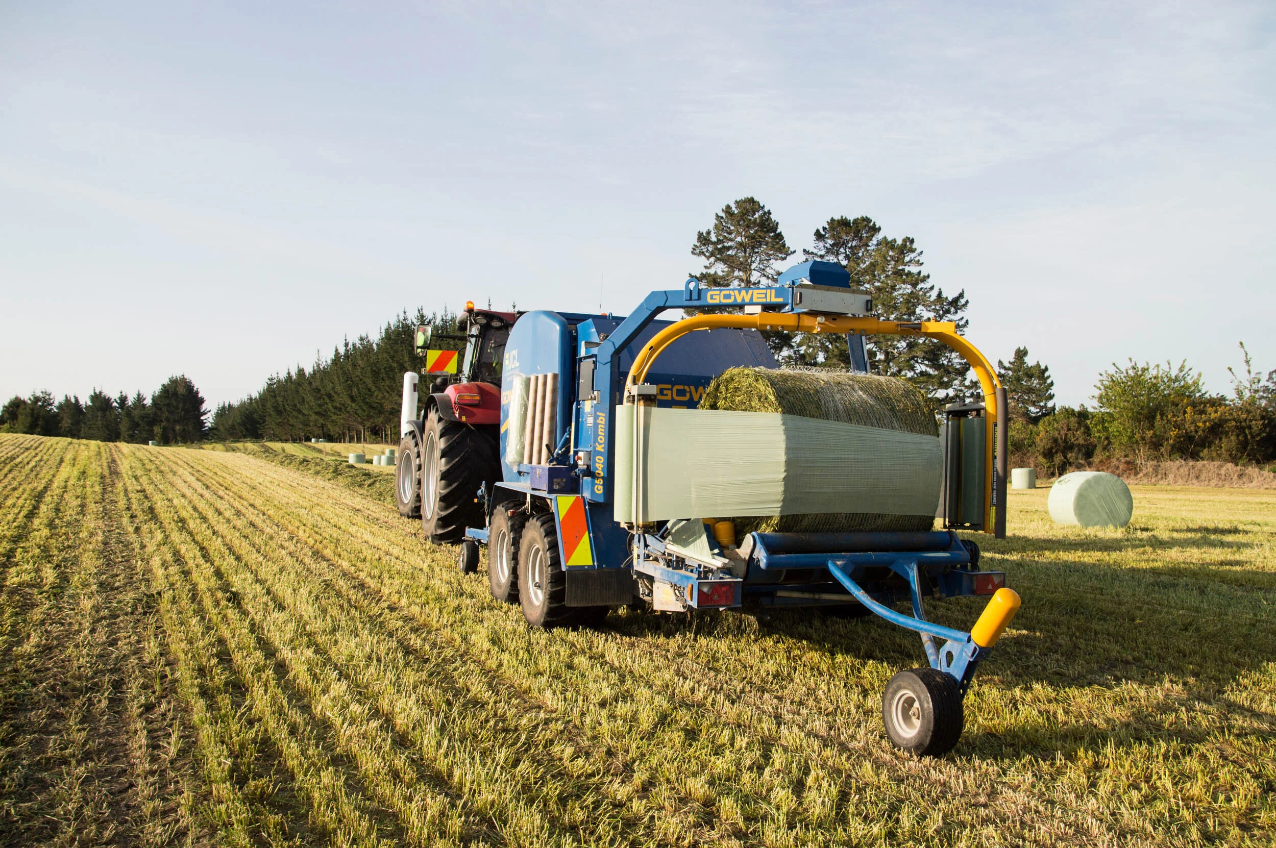 A tractor pulling a hay baler in a field of harvested crops.