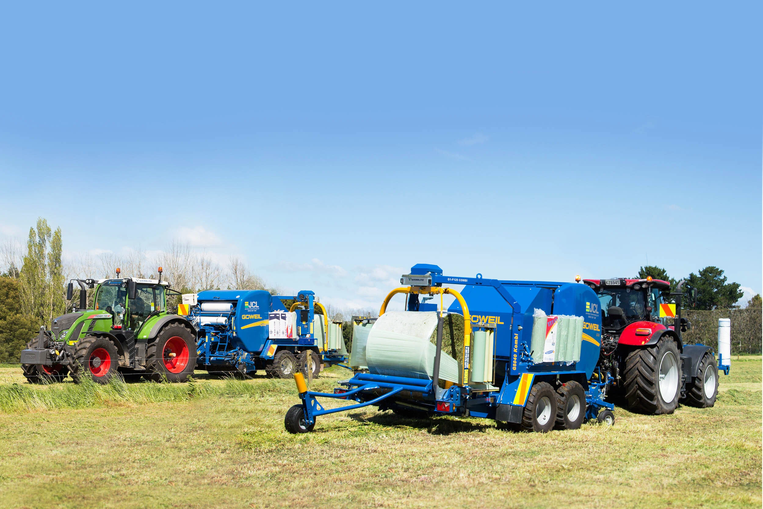 Two tractors pulling large agricultural equipment on a grassy field under a blue sky.