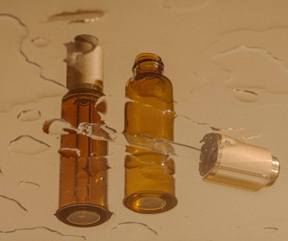 Two small amber glass bottles, one with a white cap and the other open, lying on a light-colored surface with water droplets around them.